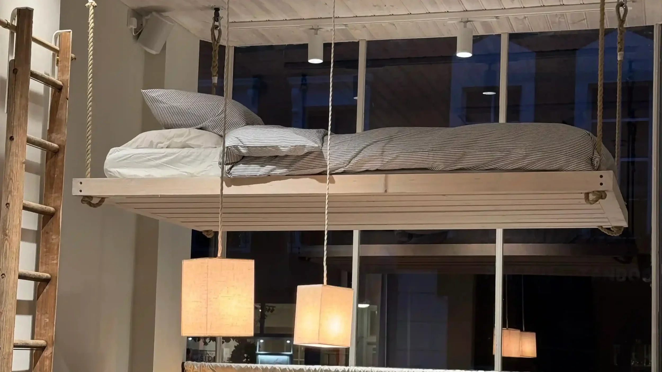 Bespoke artisan retail interior with bed suspended from ceiling by ropes, fabric pendant lighting, vintage ladder and homeware display