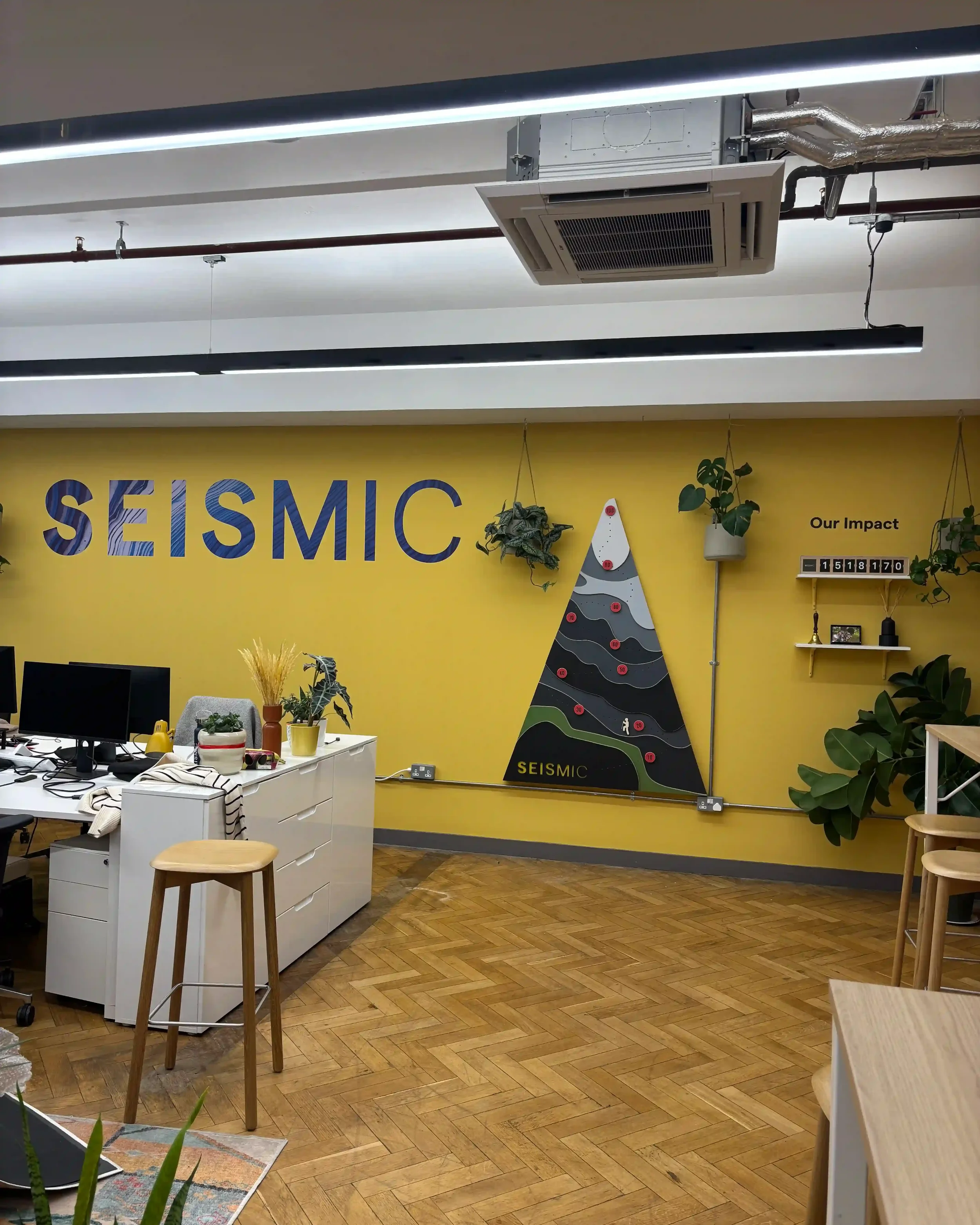 Full view of Seismic bespoke office brand installation with yellow feature wall, mountain graphic and Our Impact display shelf