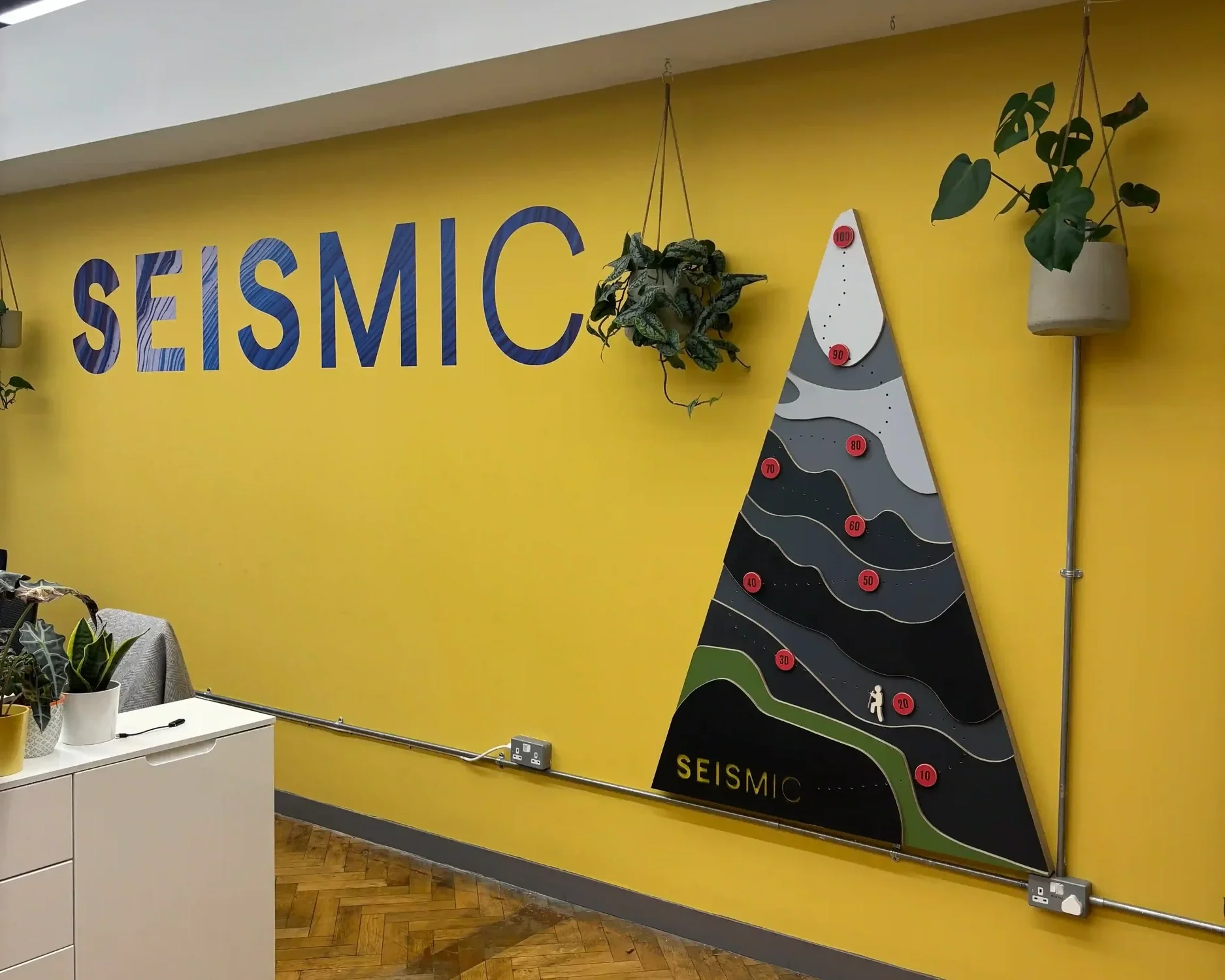 Seismic office brand installation with yellow feature wall, large branded lettering and bespoke triangular mountain display board
