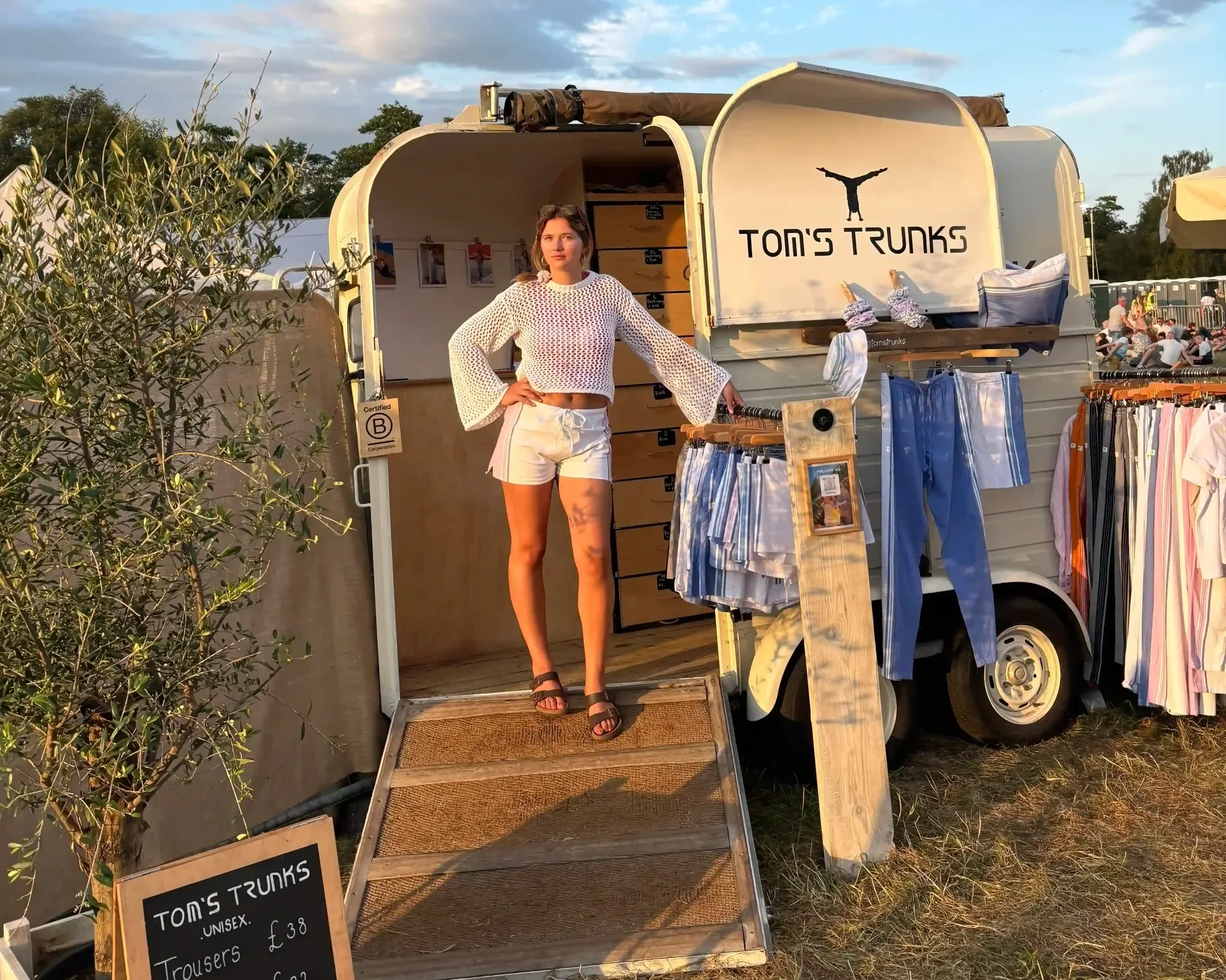 Tom's Trunks branded horsebox mobile retail brand activation at outdoor festival under dramatic sky with chalkboard pricing sign
