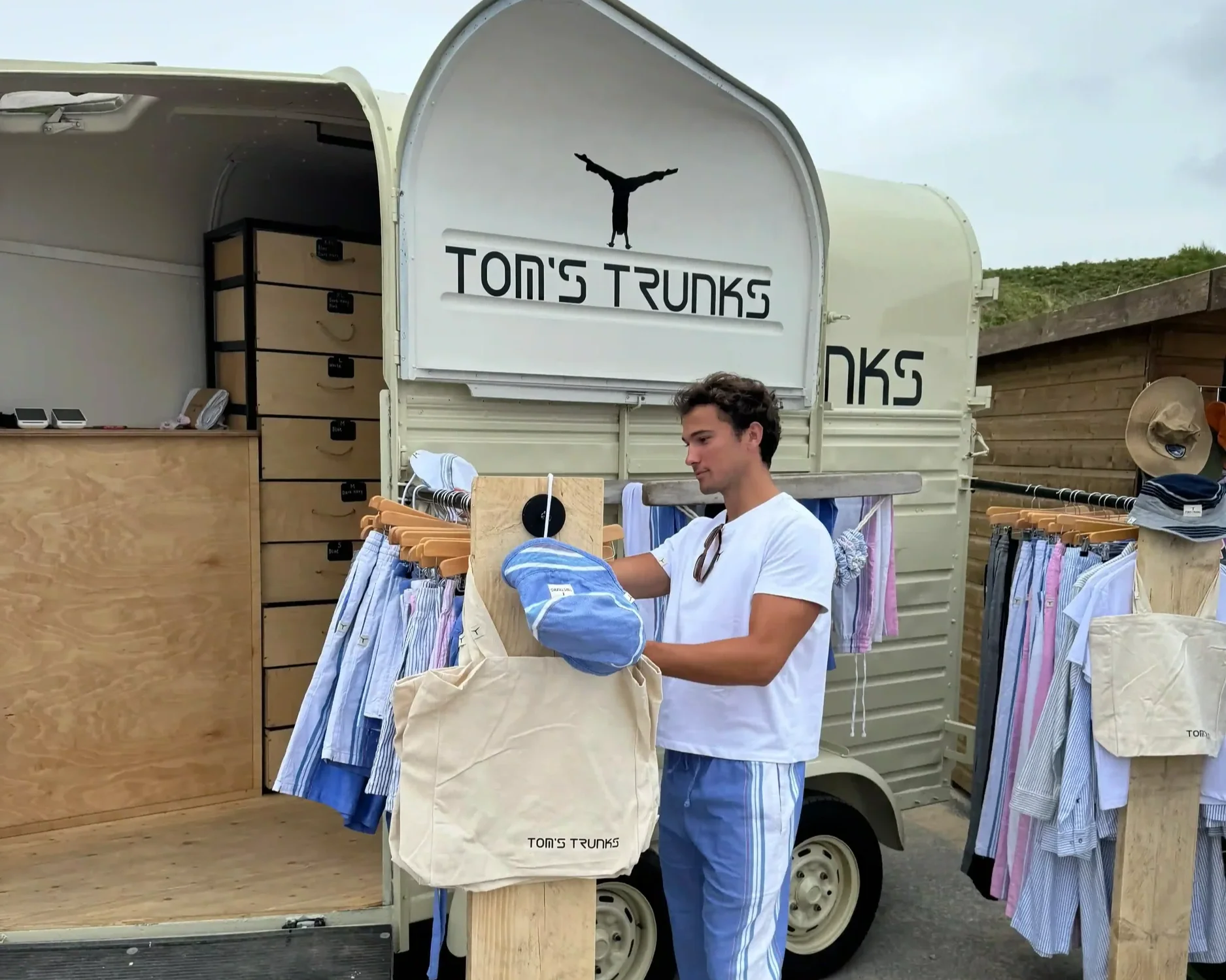 Staff member at Tom's Trunks branded horsebox mobile retail brand activation unit with clothing display racks at outdoor event