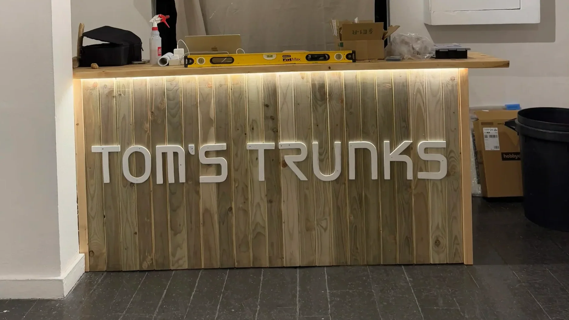 Tom's Trunks bespoke illuminated wooden counter with LED back-lit branded stencil lettering during retail fit-out installation