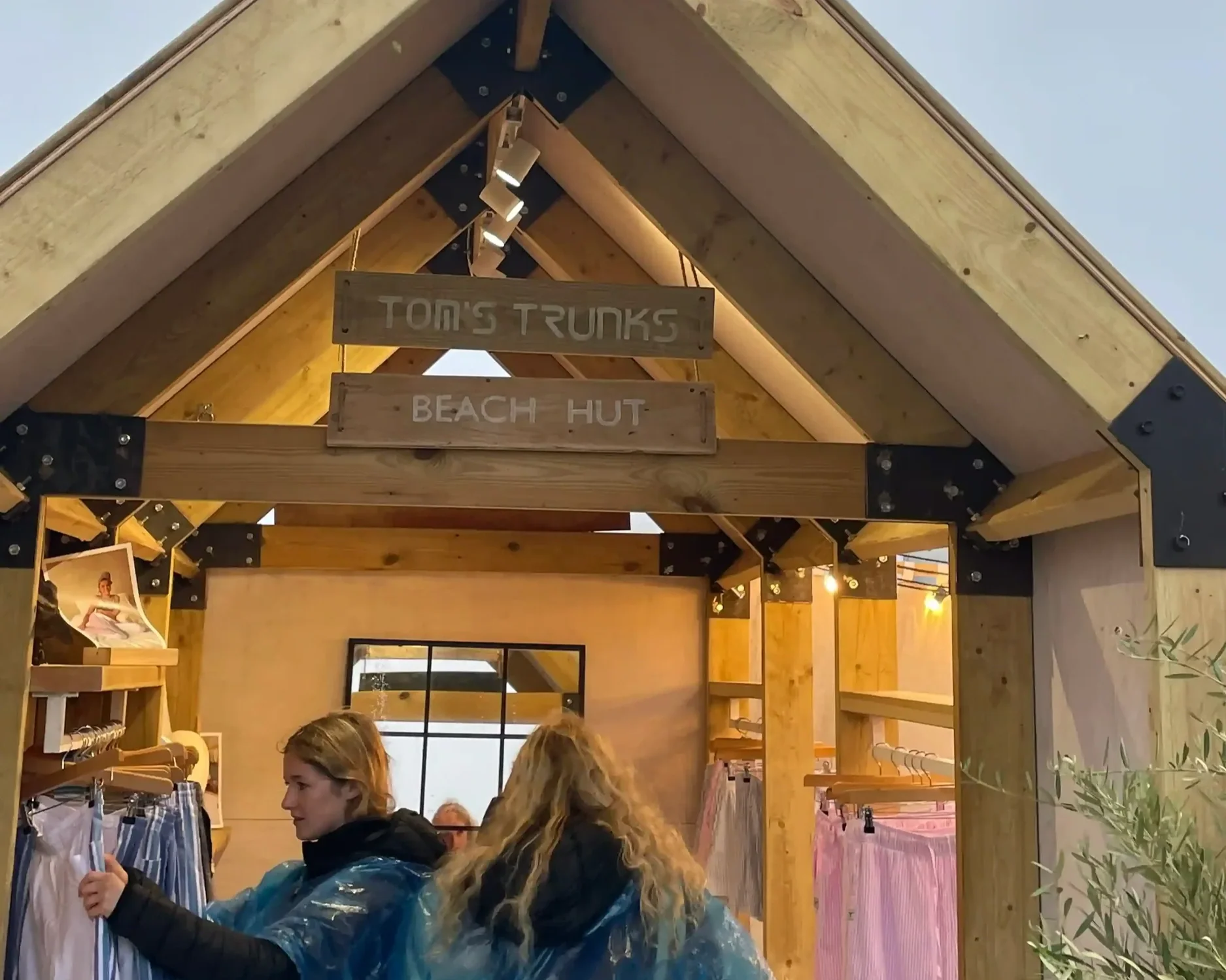 Tom's Trunks bespoke wooden beach hut brand activation structures at outdoor festival during golden sunset with potted olive trees