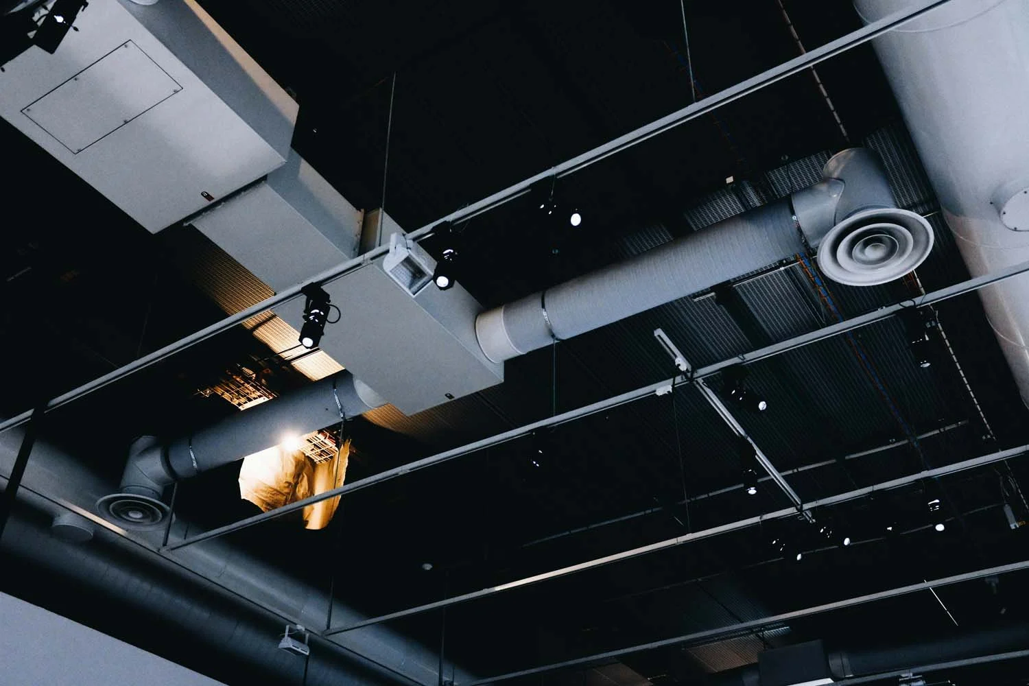 Ceiling with suspended HVAC ductwork, ventilation fans, and industrial lighting fixtures.