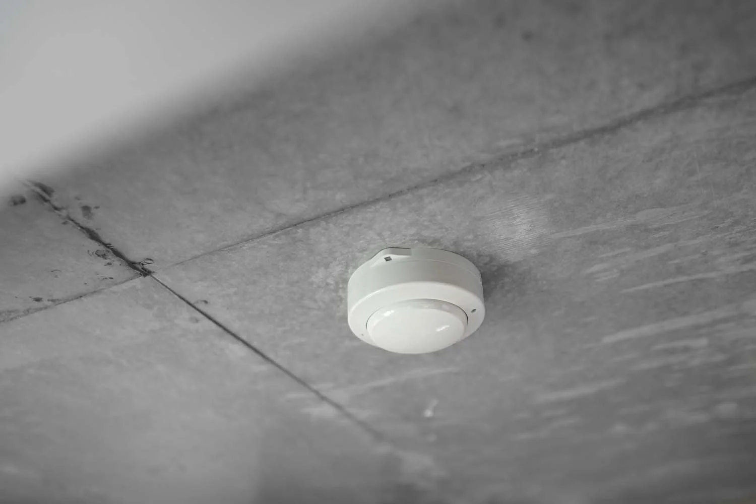 A round smoke detector mounted on a gray tiled ceiling.
