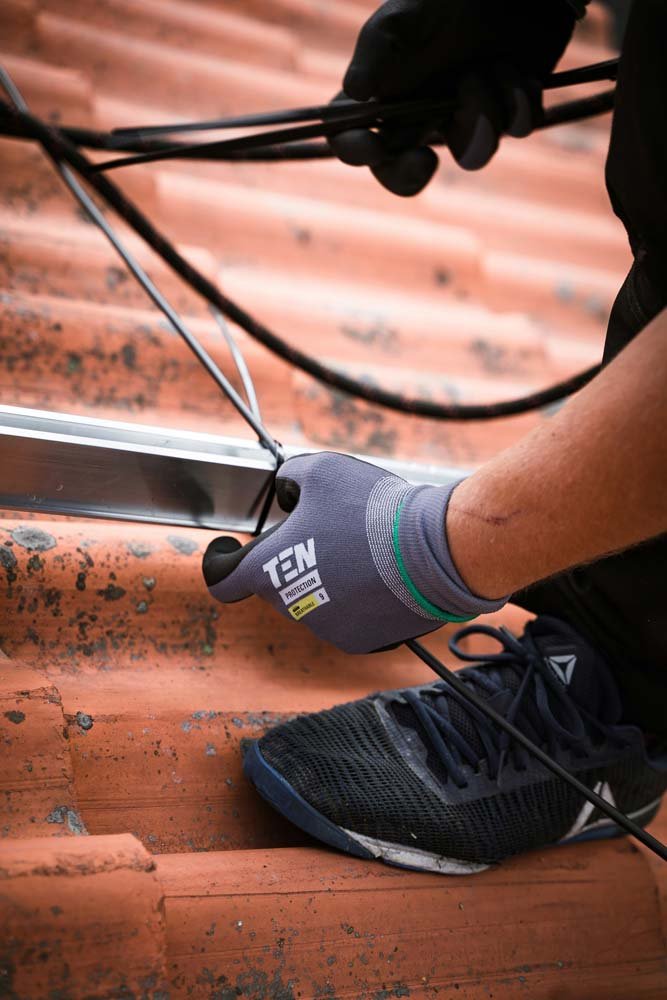 Person wearing gloves and athletic shoes working on a metal piece on a wooden surface.