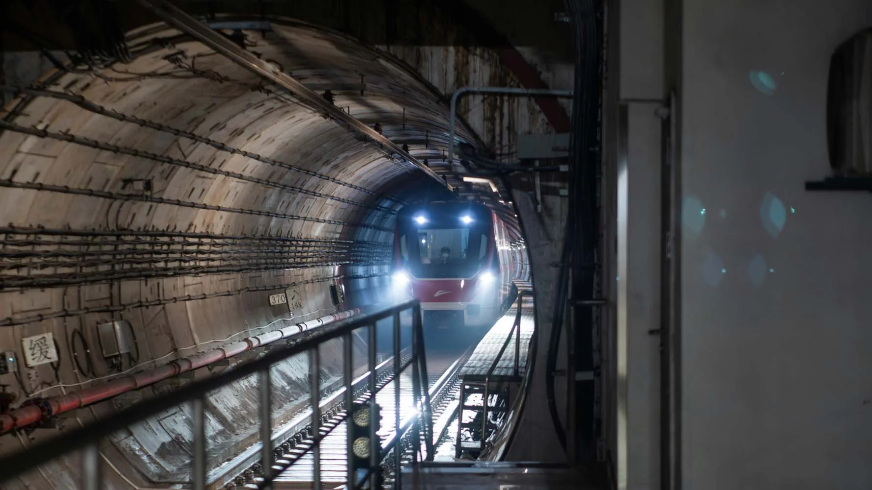 A train is emerging from a tunnel with bright headlights illuminating the dark interior.