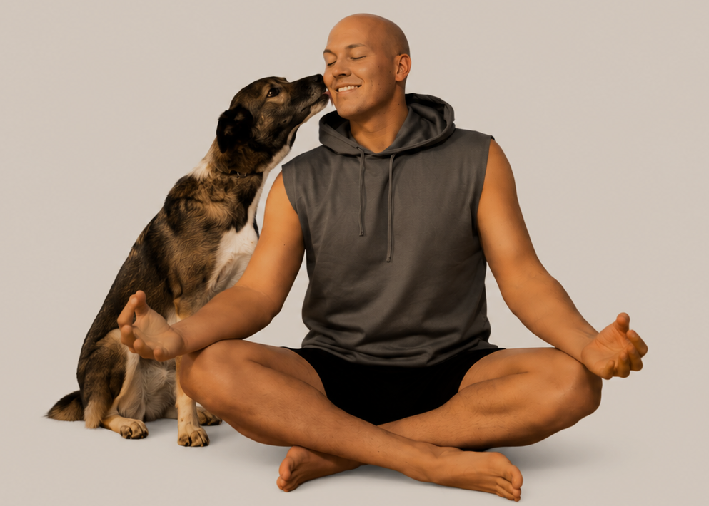 Ein Mann sitzt im Schneidersitz auf dem Boden in einer Yogapose, während ein Hund ihm einen Kuss auf die Wange gibt. Der Mann lächelt zufrieden.