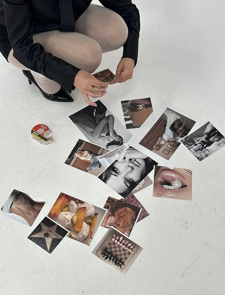 Person sitting on the floor with legs folded, sorting through various photographs and images scattered on the white ground.