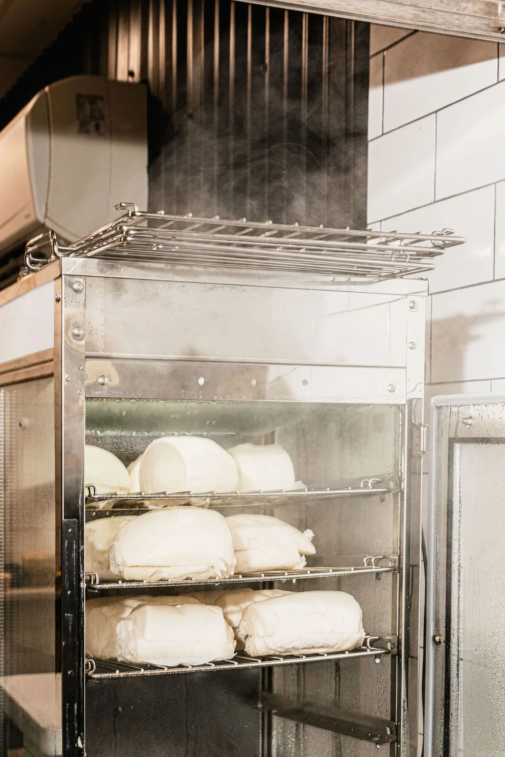 Cheese blocks stored inside a stainless steel refrigerated showcase in a kitchen.