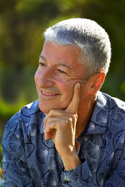 Homme âgé souriant, pensif, dehors, en plein air, soleil, vêtement à motifs floraux bleus.