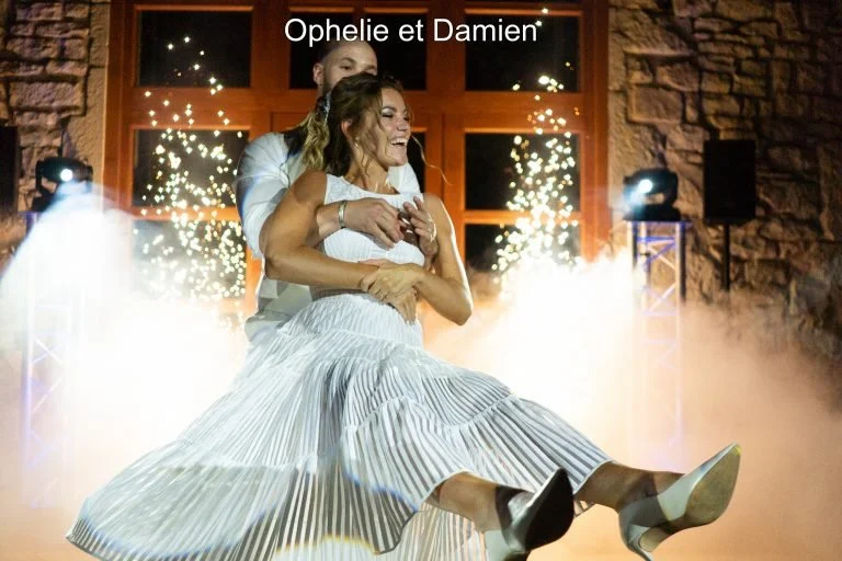 Un couple en robe de mariée et costume en train de danser lors de leur mariage, avec des lumières et de la fumée en arrière-plan.