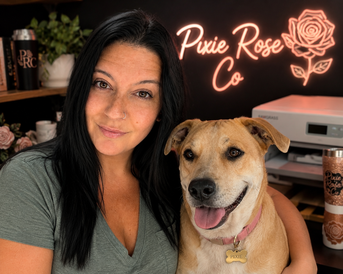 A woman with long black hair and a nose ring takes a selfie with her tan and white dog named Pixie, in a room with a neon sign that reads 'Pixie Rose Co.' and a background of books, plants, and pink roses.