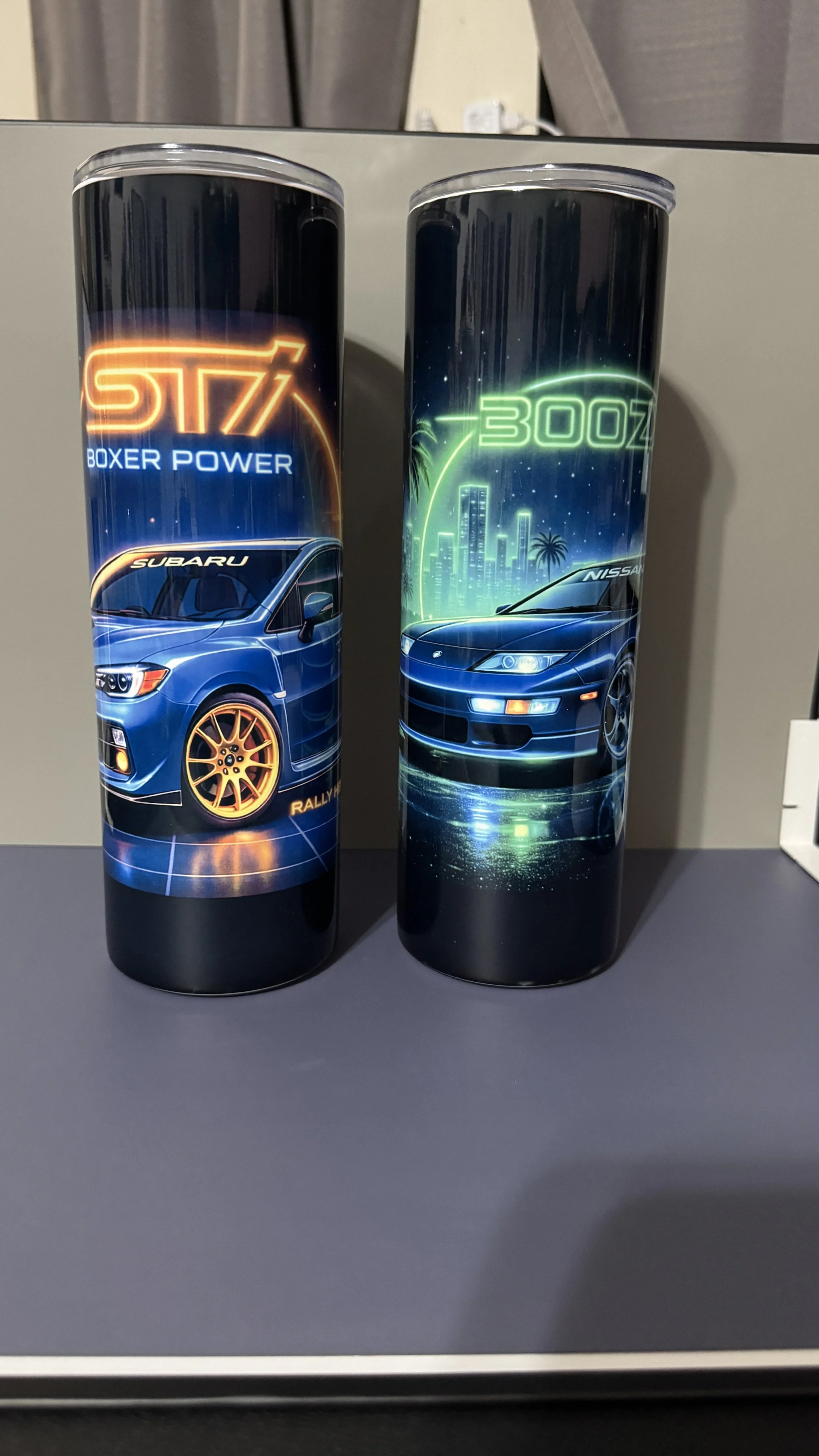 Two tall cylindrical containers with neon-style designs. The left container features a blue Subaru car with the words 'STI Boxer Power' and 'Rally X.' The right container displays a blue Nissan car with neon cityscape and palm trees, along with the t