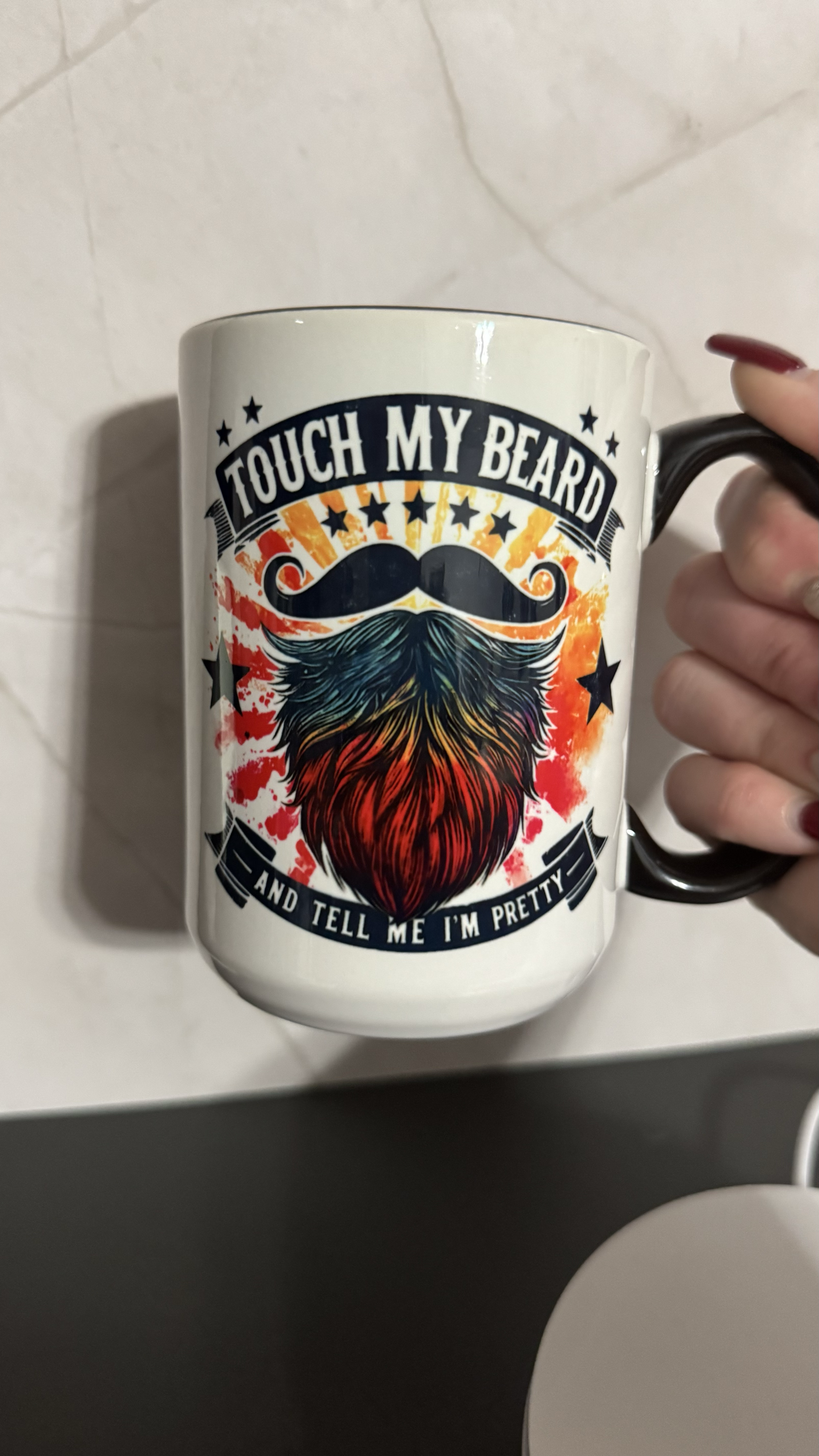 A white coffee mug with a design of a beard and mustache with the text 'Touch my beard and tell me I'm pretty' on it.
