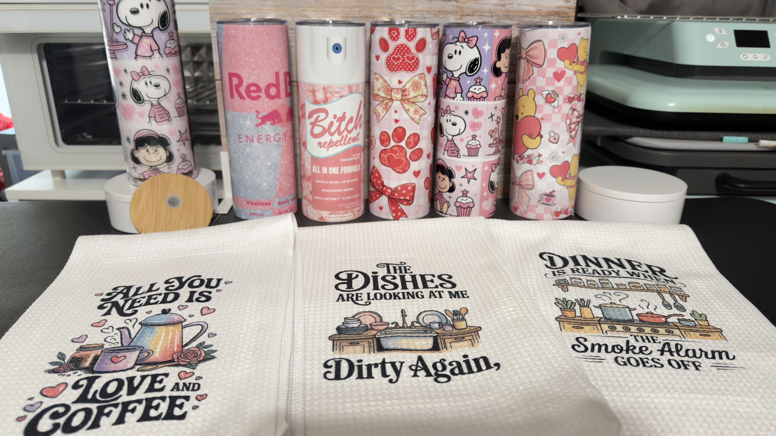 Set of seven decorated cans with cartoon characters and patterns, placed on a black surface in front of kitchen-themed dish towels with inspirational quotes.