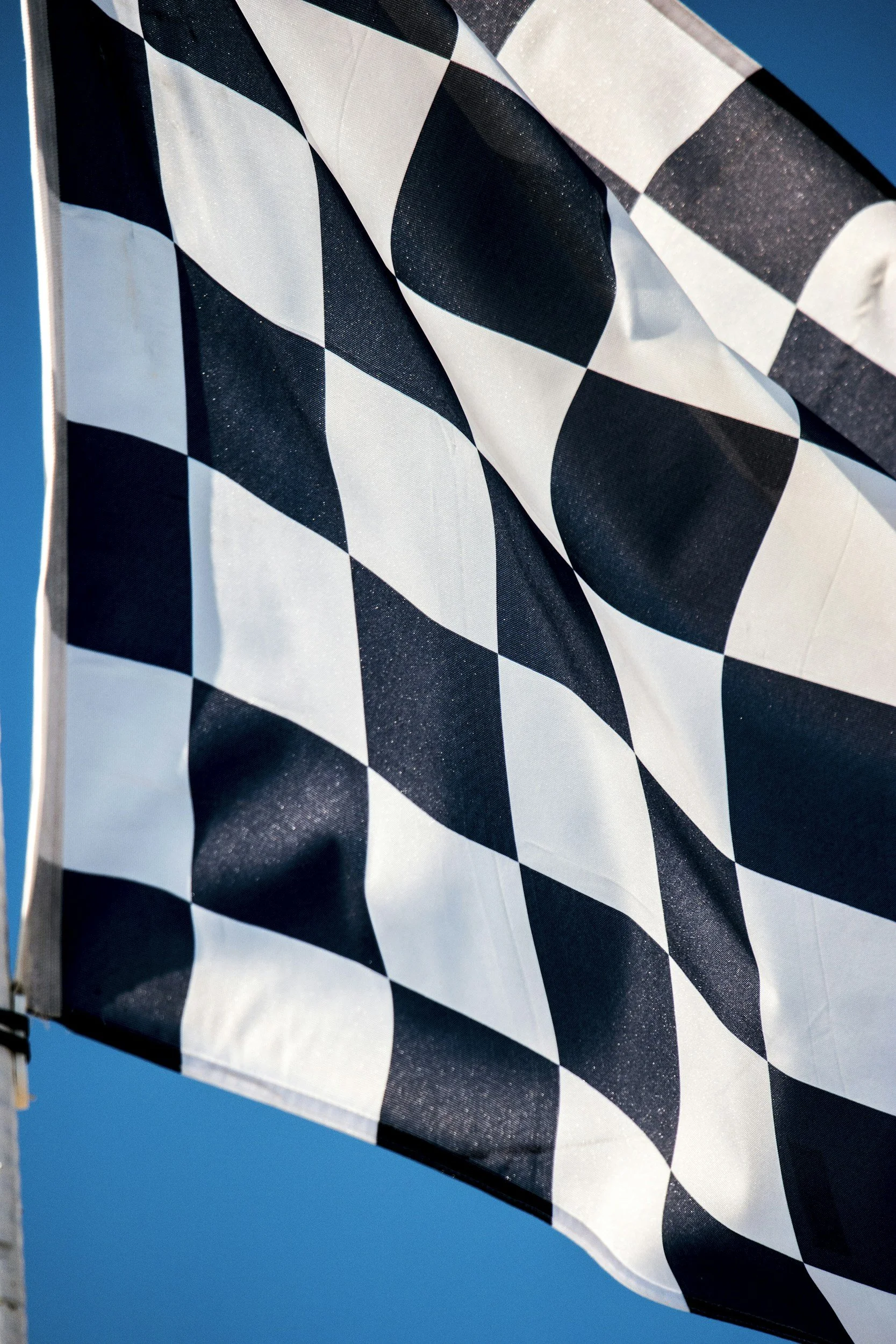 A black and white checkered flag waving against a bright blue sky.