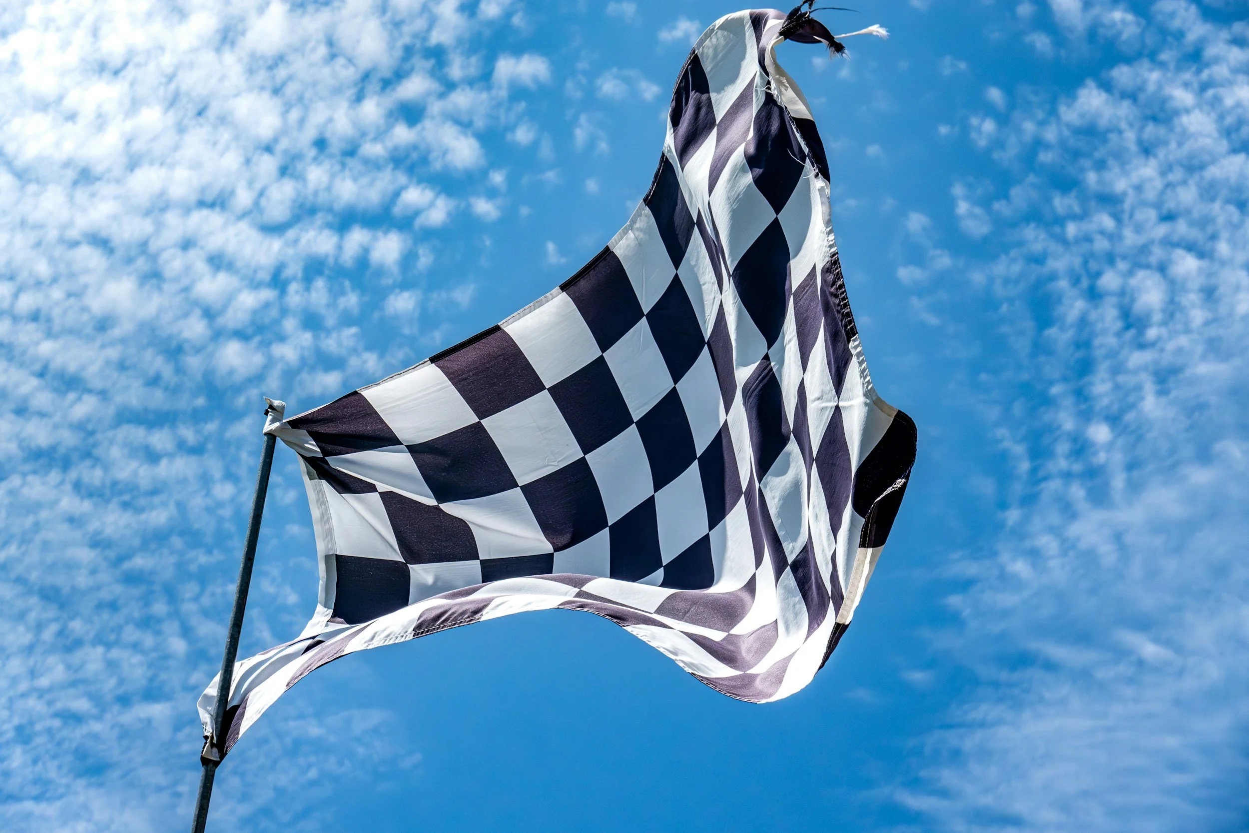 A checkered black and white racing flag waving in the wind against a cloudy blue sky.