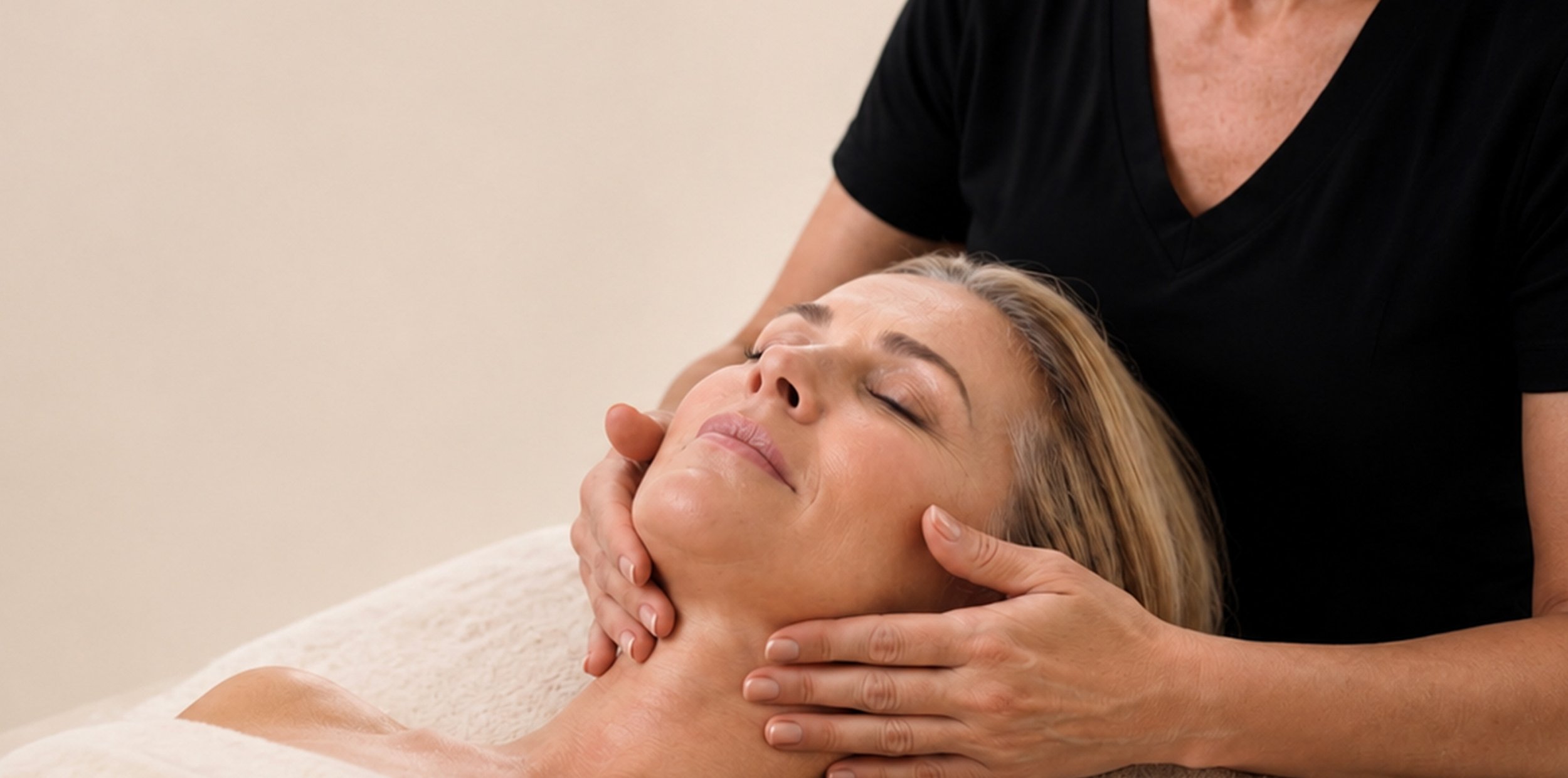 A woman is receiving a facial massage or therapy from a therapist in a treatment room.