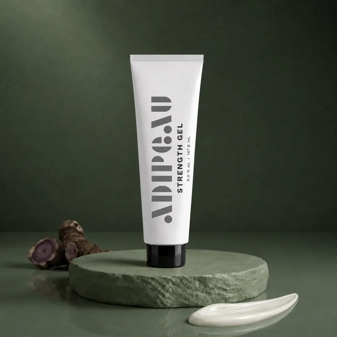 A tube of Dr. Jart+ Strength Gel standing on a round green stone platform with a piece of ginger root and a dollop of cream nearby, against a green background.