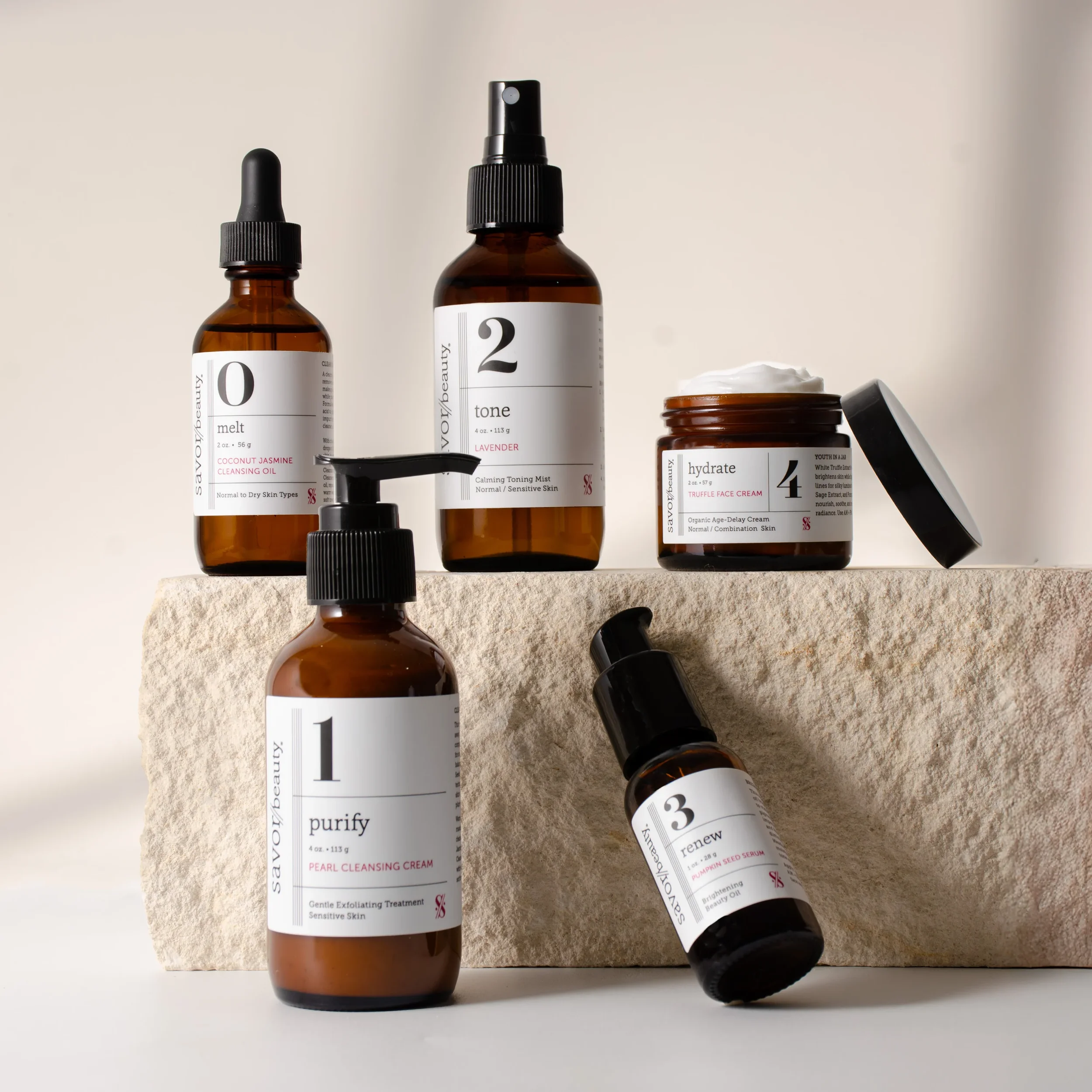 Several skincare bottles and jars with brown glass and white labels, set on a textured surface against a light background.
