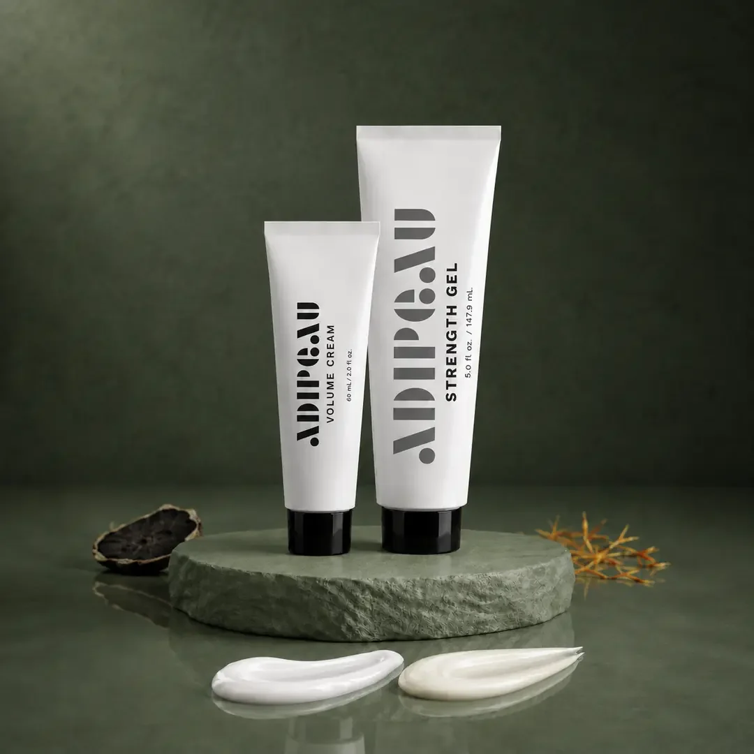 Two skincare tubes labeled 'ADDIP.DU' with one for volume cream and the other for strengthening gel, positioned on a round stone platform with a dried leaf and shell nearby.