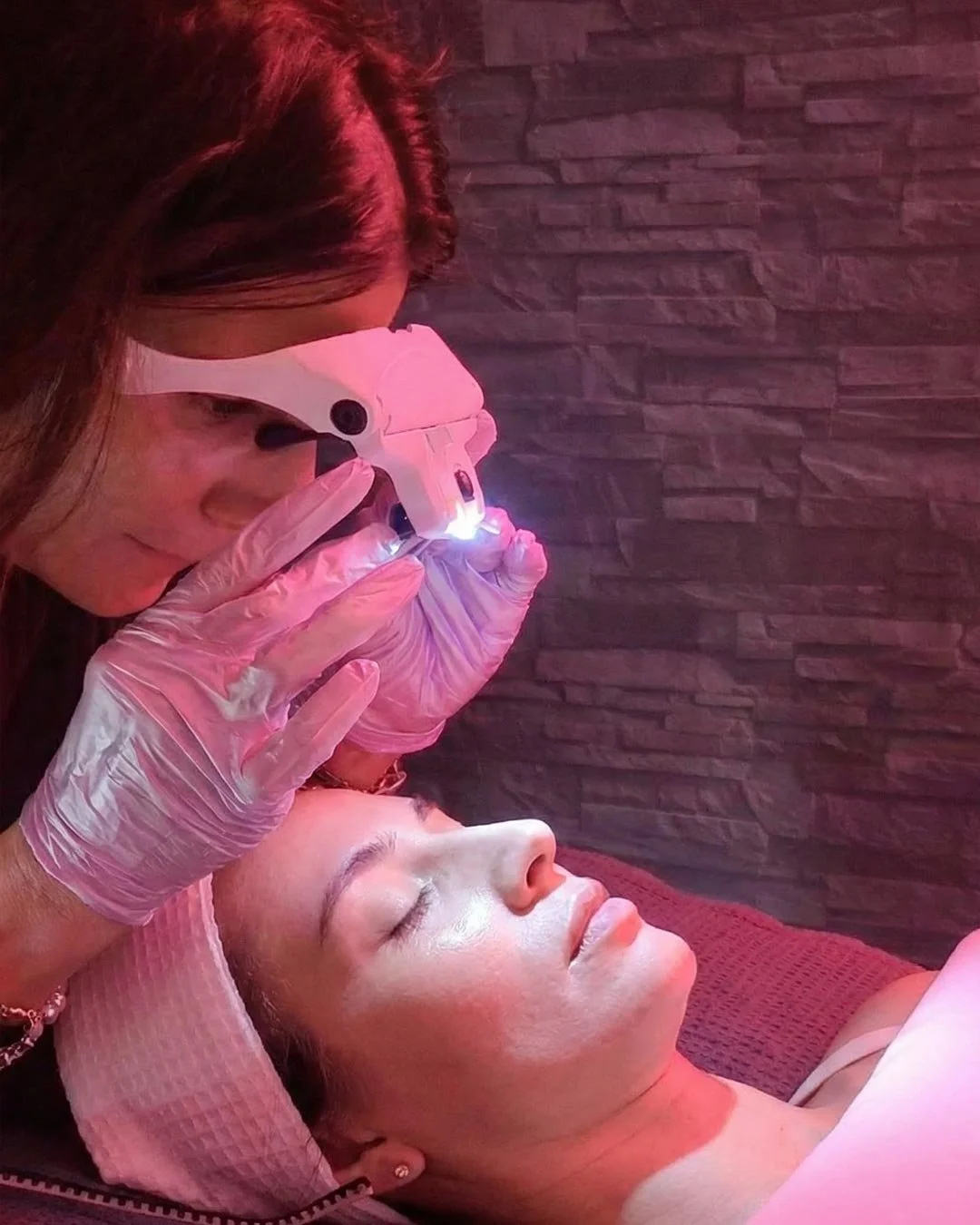 A woman receiving a cosmetic treatment from a professional using a specialized device on her forehead in a spa or clinic setting.