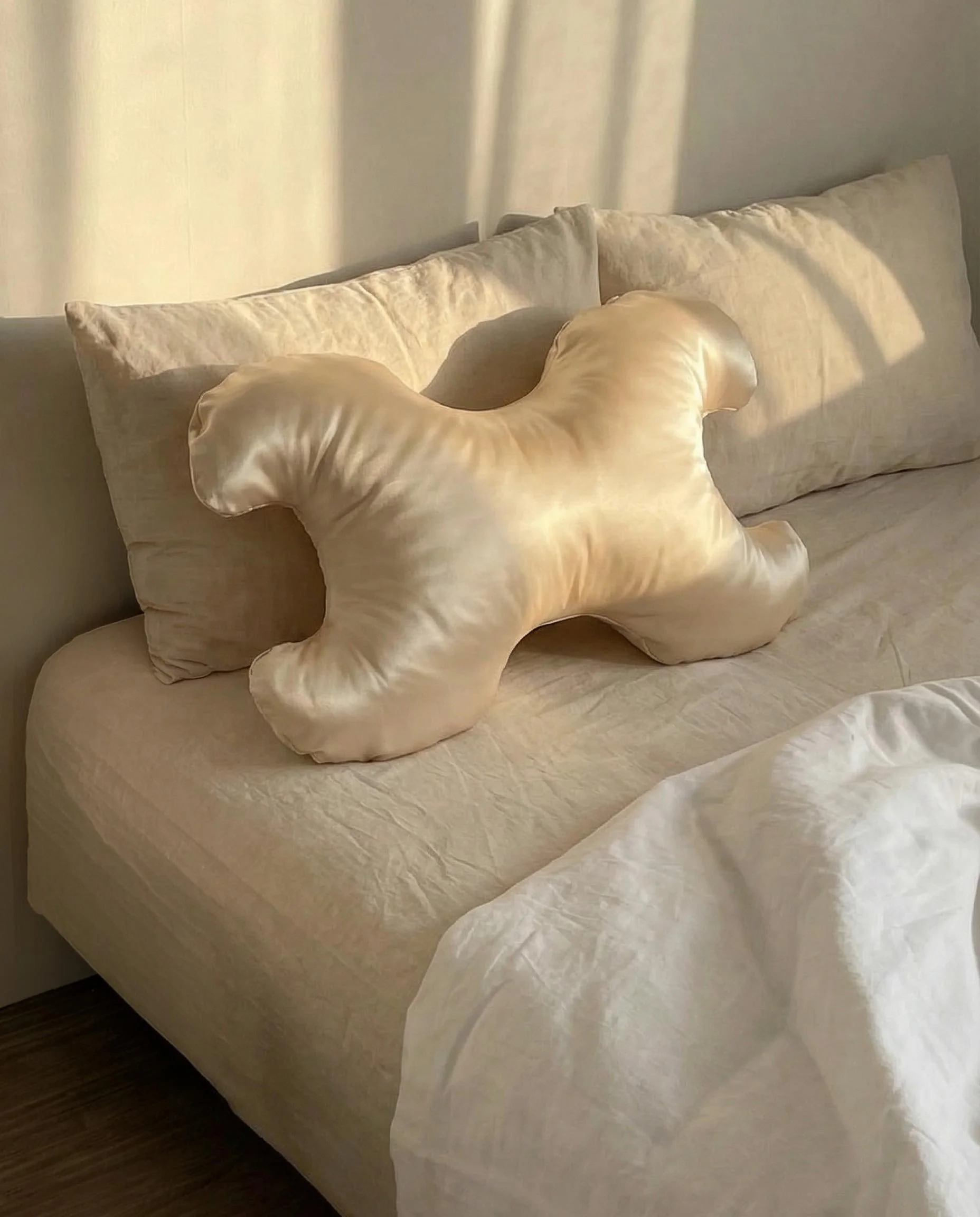 Cream-colored bed with matching pillows and a blanket, sunlight casting shadows on the wall behind the bed.