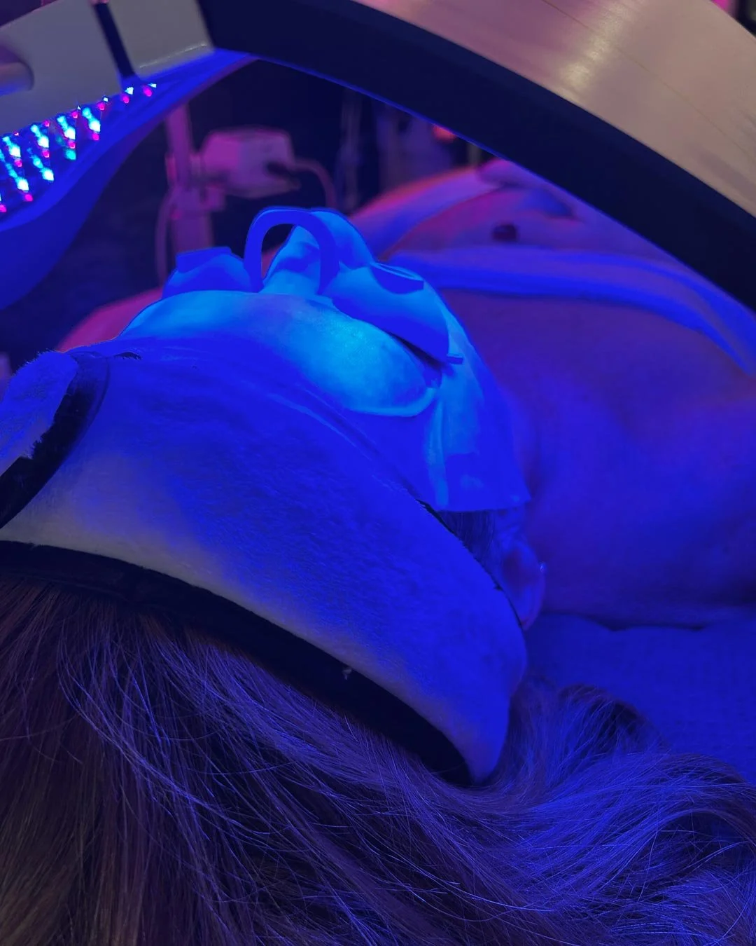 Person lying on a medical or aesthetic procedure table under blue lighting, possibly undergoing a cosmetic or dermatological treatment with head and face covered with a cloth or mask.