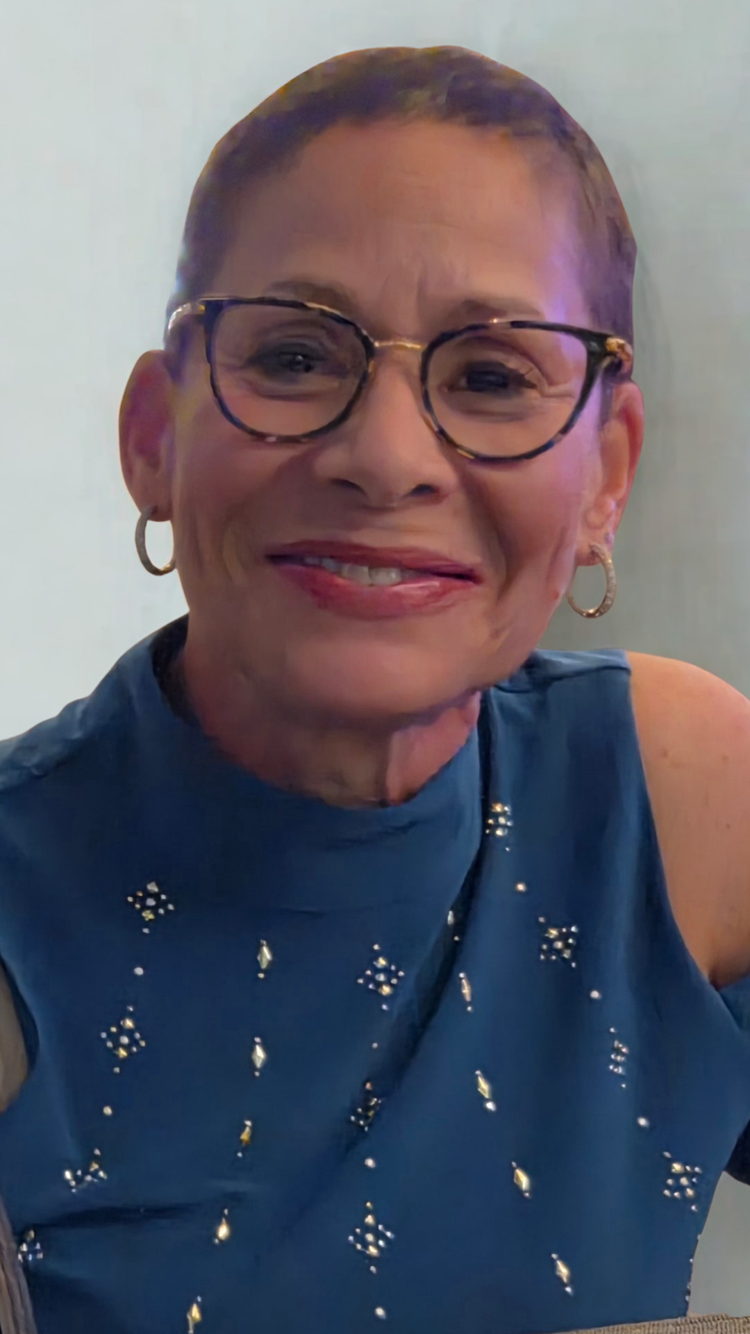 Chef Wayne G. Hooker Scholarship founder A woman with glasses and earrings smiling in a dark blue dress with silver embellishments.