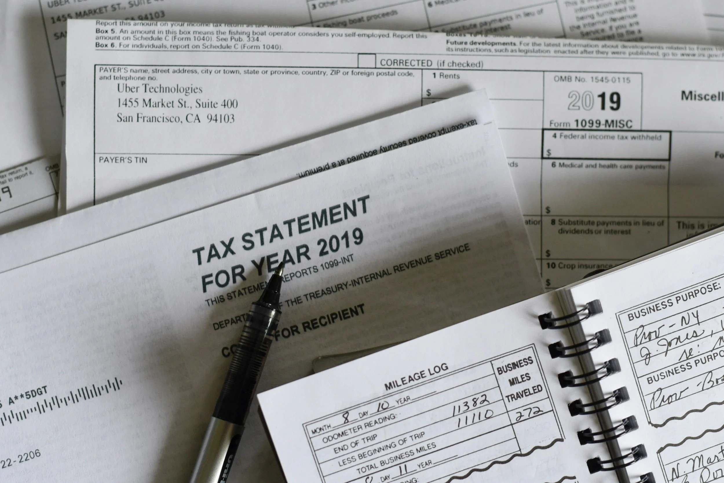 A collection of tax documents and a pen on a table. The documents include forms for income tax reporting and a handwritten note.