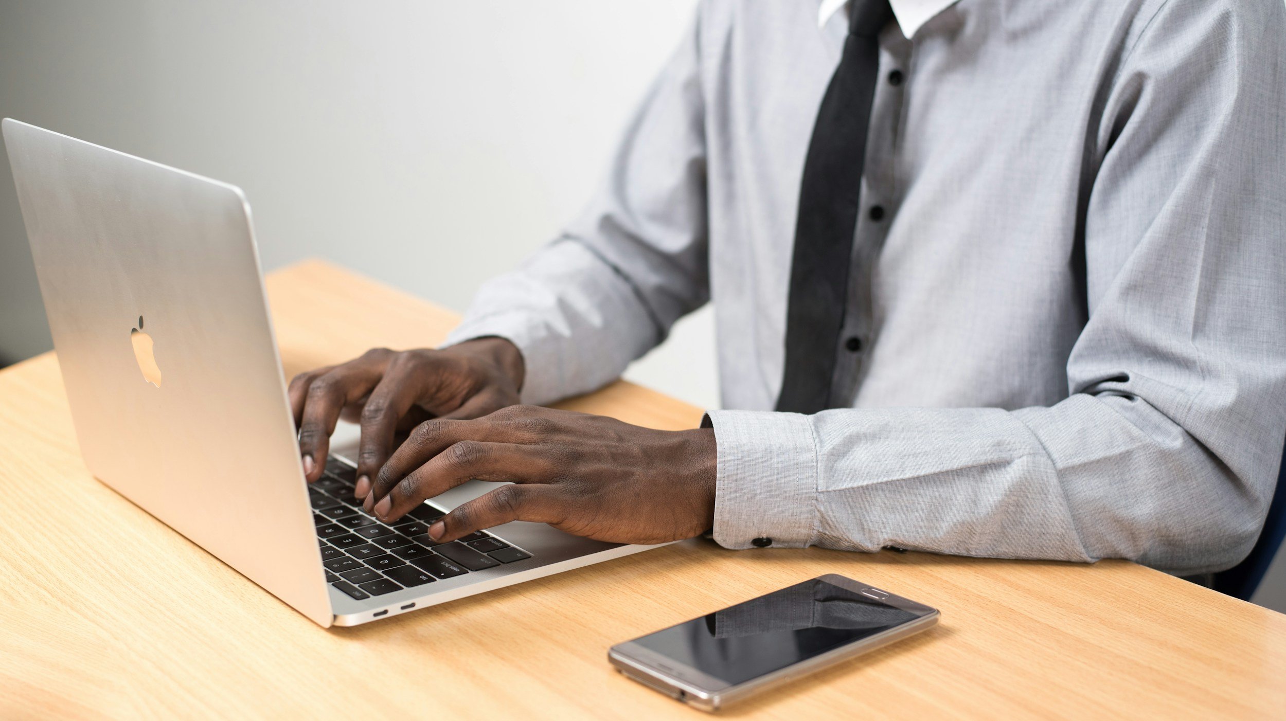 Person working on a MacBook at a wooden desk with a smartphone nearby.