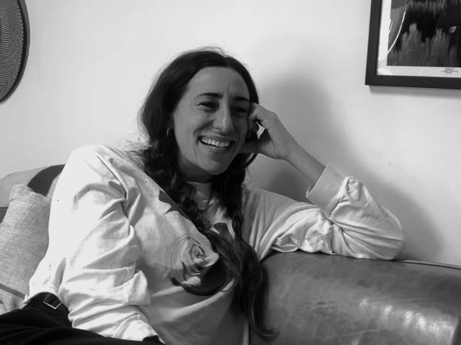 Femme assise sur un canapé, souriante et détendue, en black et white, avec une œuvre d'art sur le mur en arrière-plan.