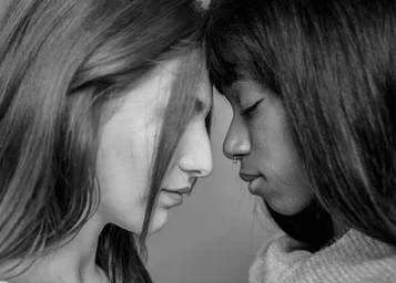 Deux jeunes filles se regardent face à face avec les fronts presque touchants, en noir et blanc.