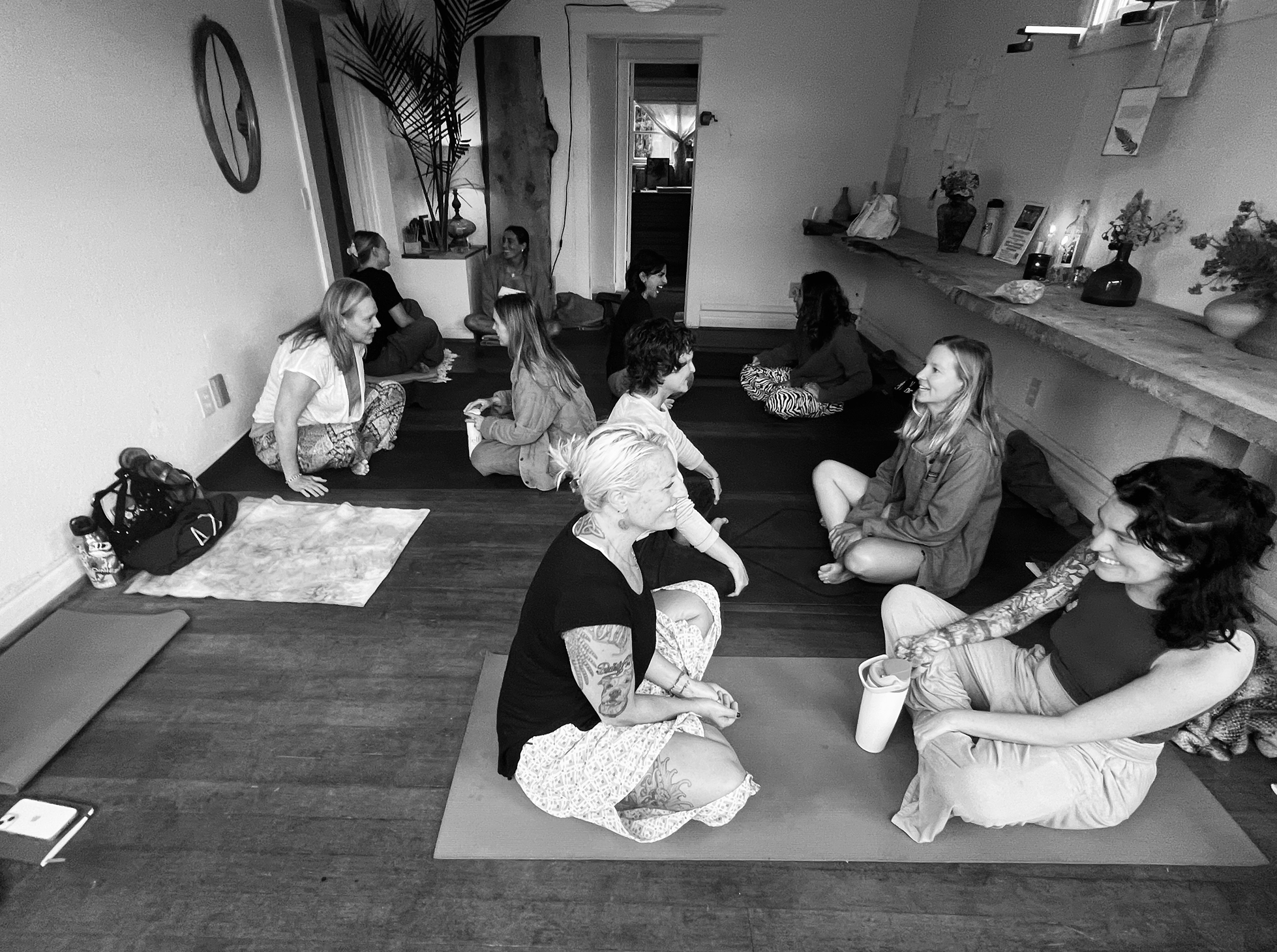 Groupe de personnes assises en cercle sur le sol dans une pièce, participant à une séance de méditation ou de discussion en groupe.