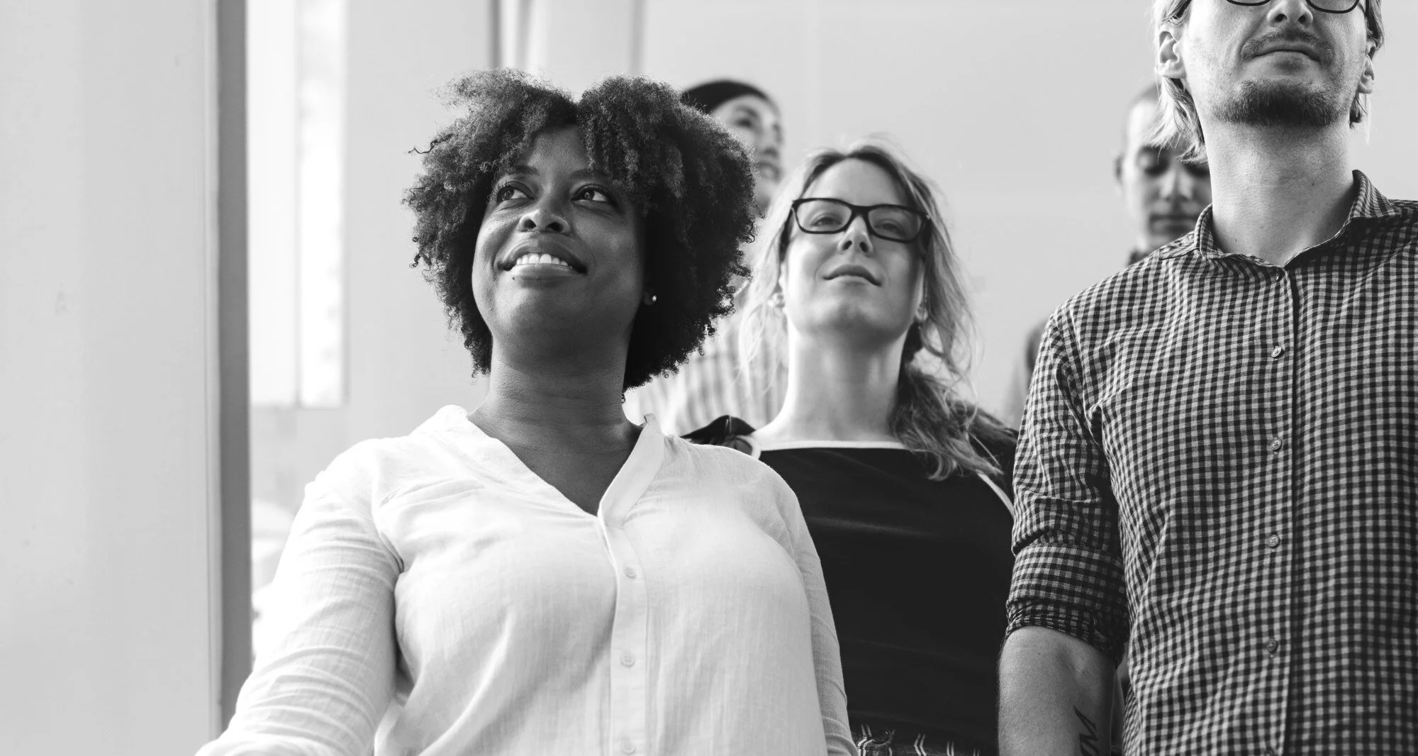 Groupe de personnes diverses, principalement des femmes, debout et regardant vers l'avant, dans une salle