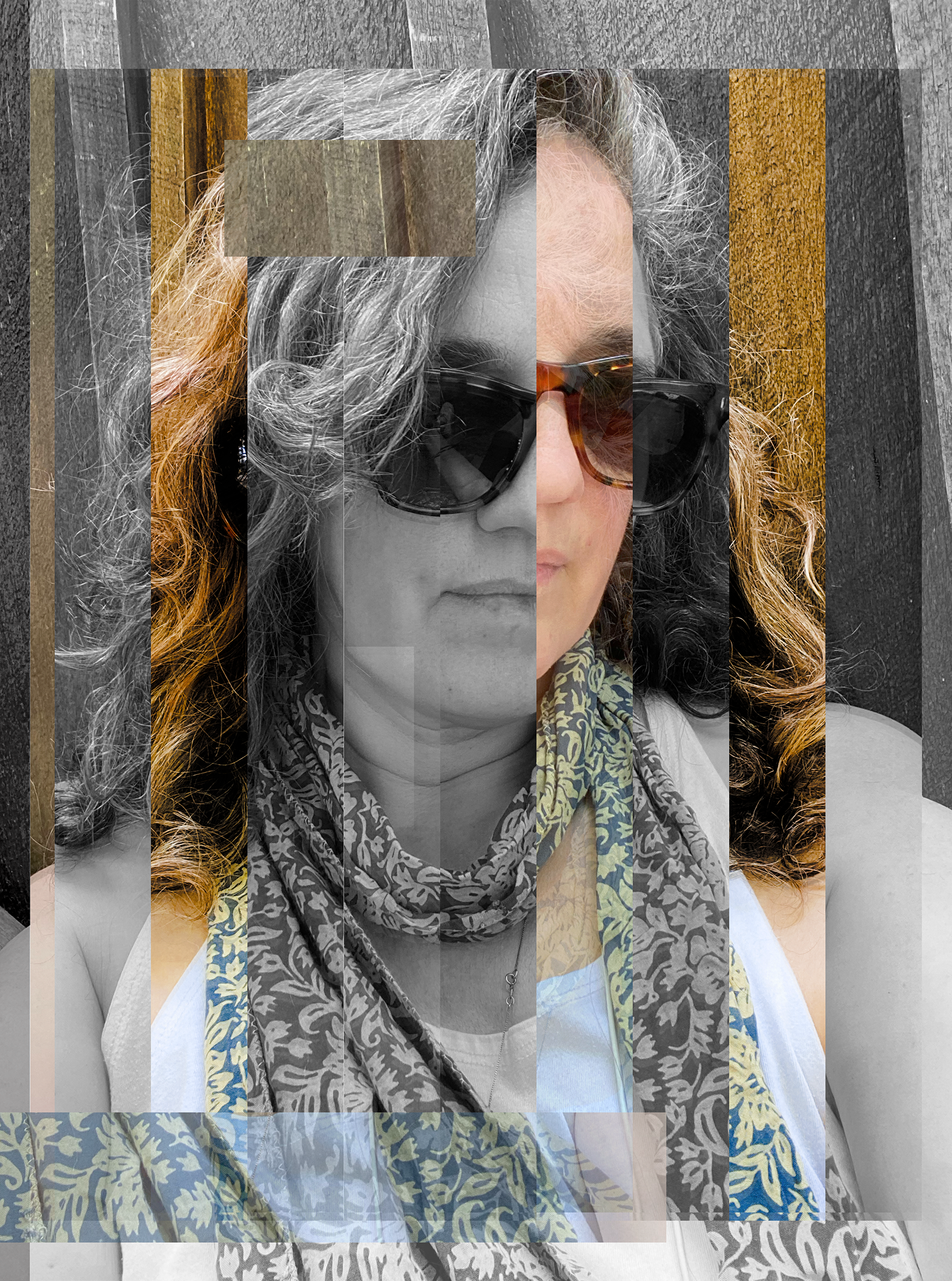 A woman with gray curly hair wearing sunglasses, a patterned scarf, and a white sleeveless top, posed outdoors against a wooden background.