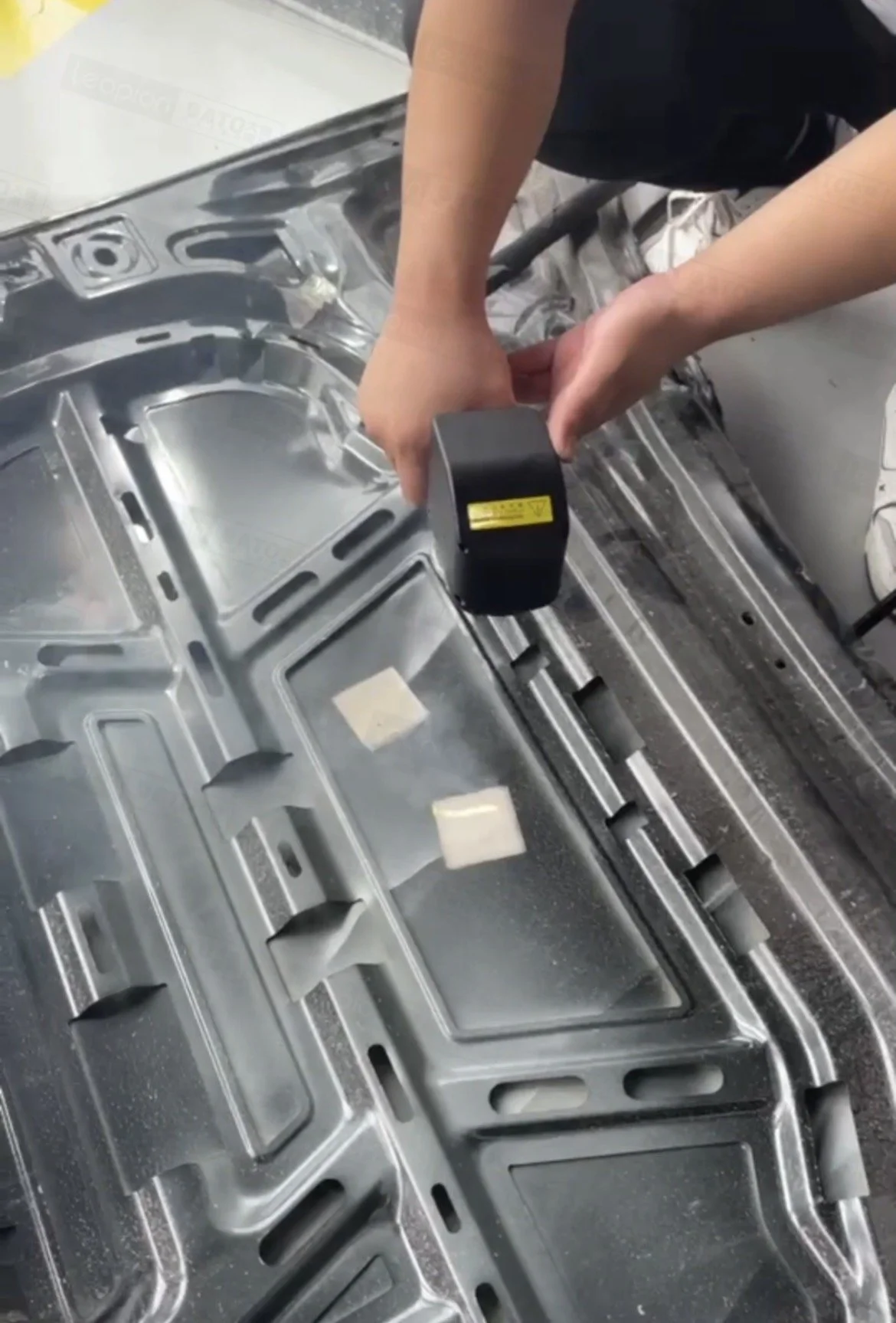 A person using a rubber mallet on a metal car door frame inside a workshop.