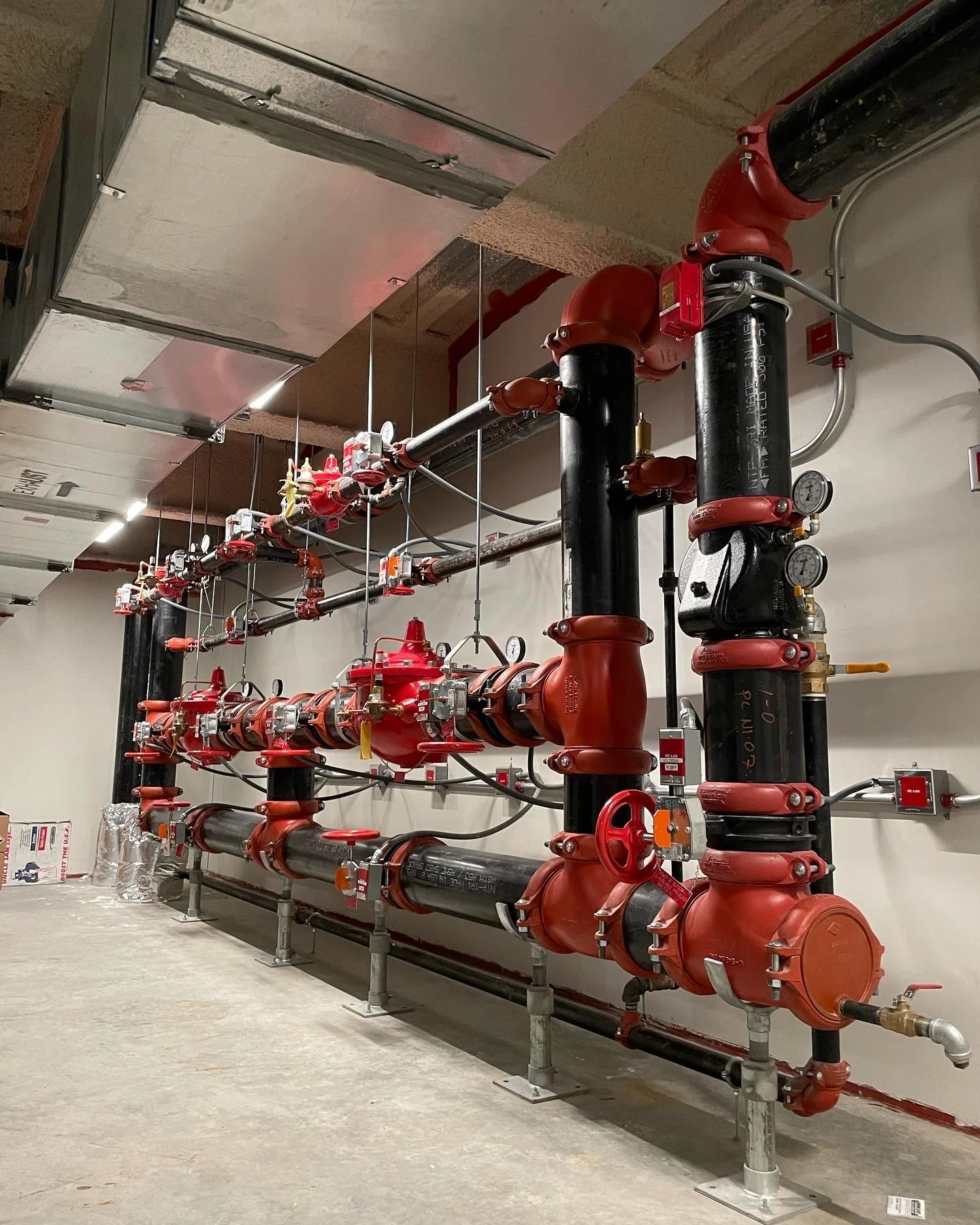 Industrial piping system with large black pipes, red valves, and gauges in a construction setting.