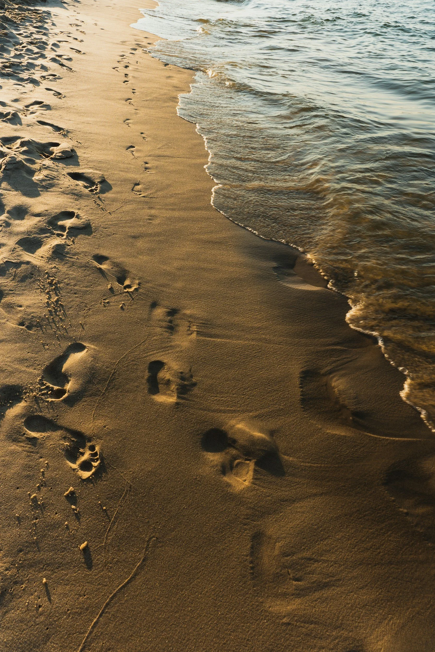 Footprints in the sand at the beach with gentle waves coming ashore