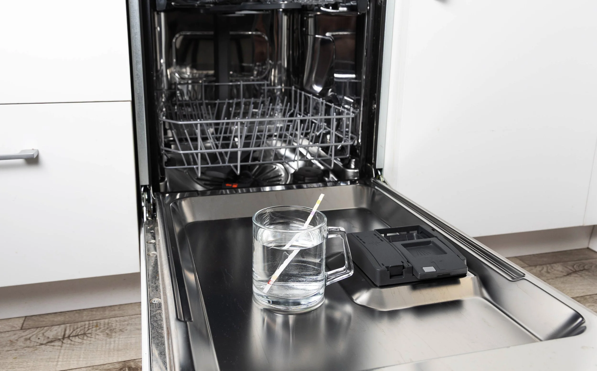An open dishwasher with the dishes inside and a glass of water with a straw on the countertop in front of it.