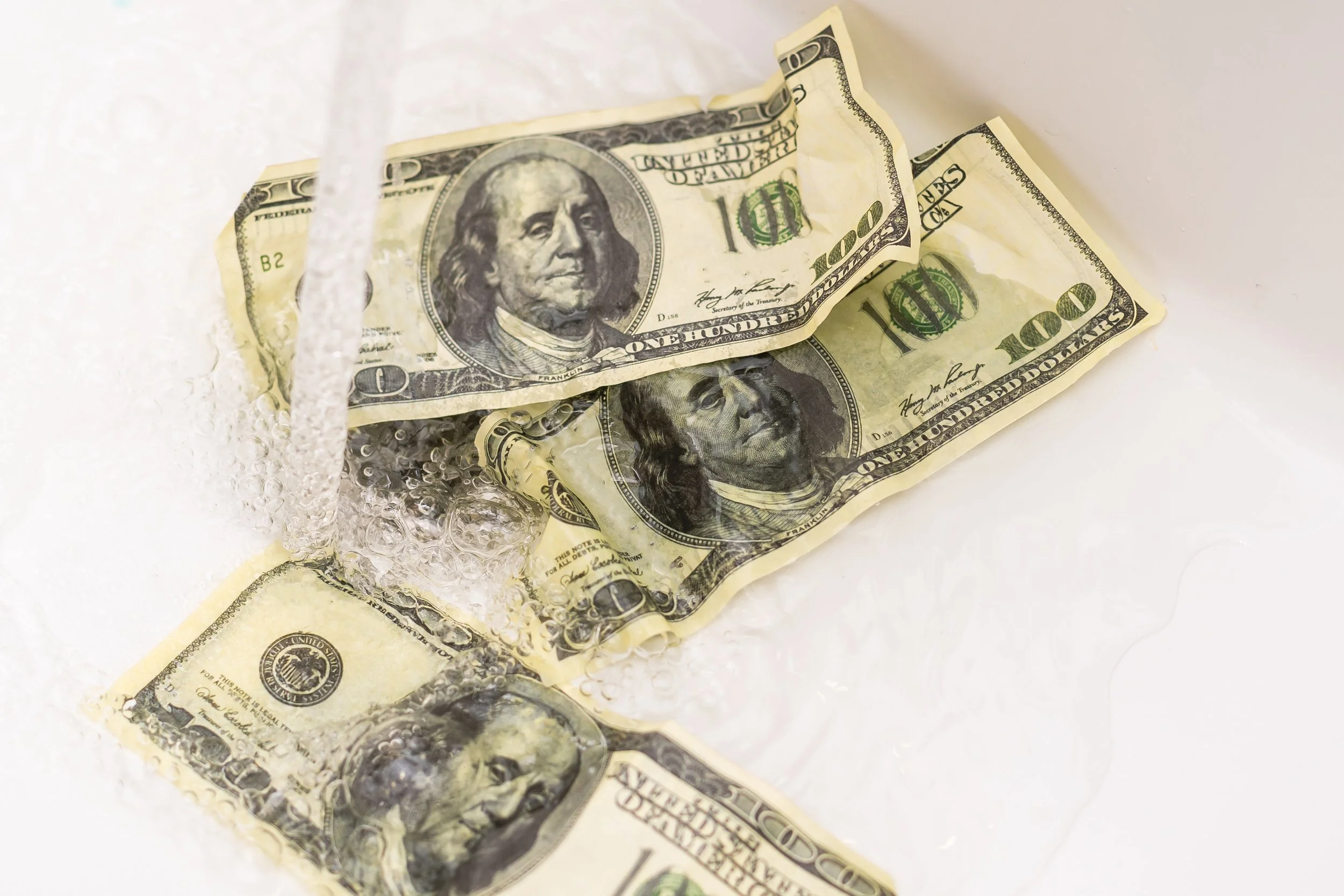 Wadded and crumpled ten-dollar bills being placed into or taken out of a transparent plastic bag, with bubbles of air visible around the money.