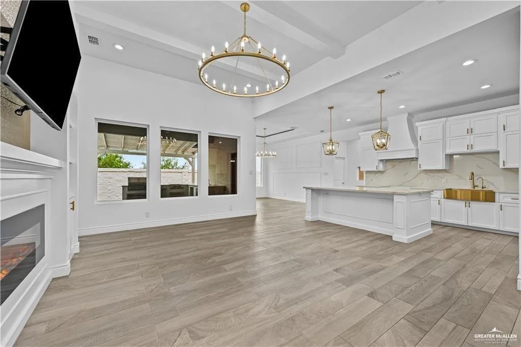 Open-concept kitchen and living room with white cabinetry, hardwood flooring, a chandelier, and a wall-mounted TV.