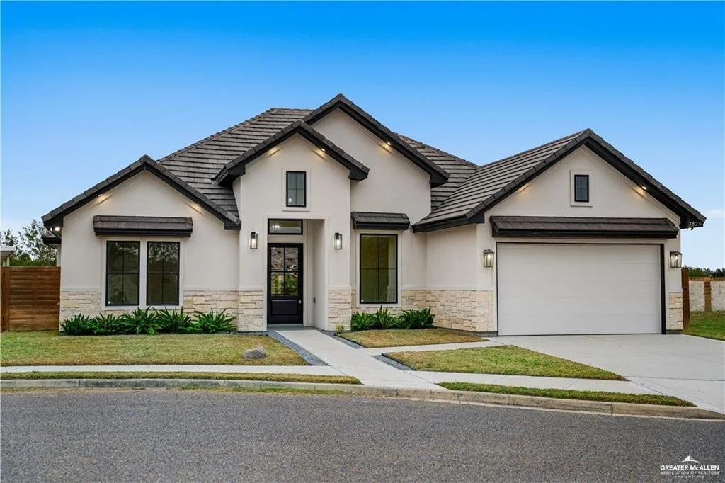 Modern single-family house with a two-car garage, white exterior walls, stone accents, a small front porch, and landscaped yard under a blue sky.