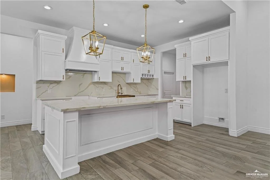 Modern white kitchen with marble countertops, gold fixtures, and pendant lights.