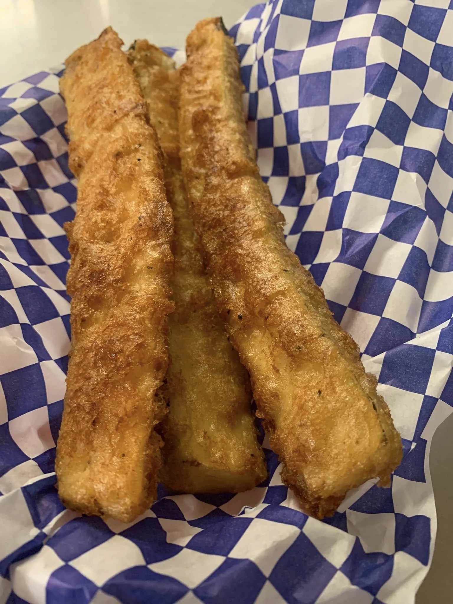 Three golden-brown fried fish fillets on checkered paper.