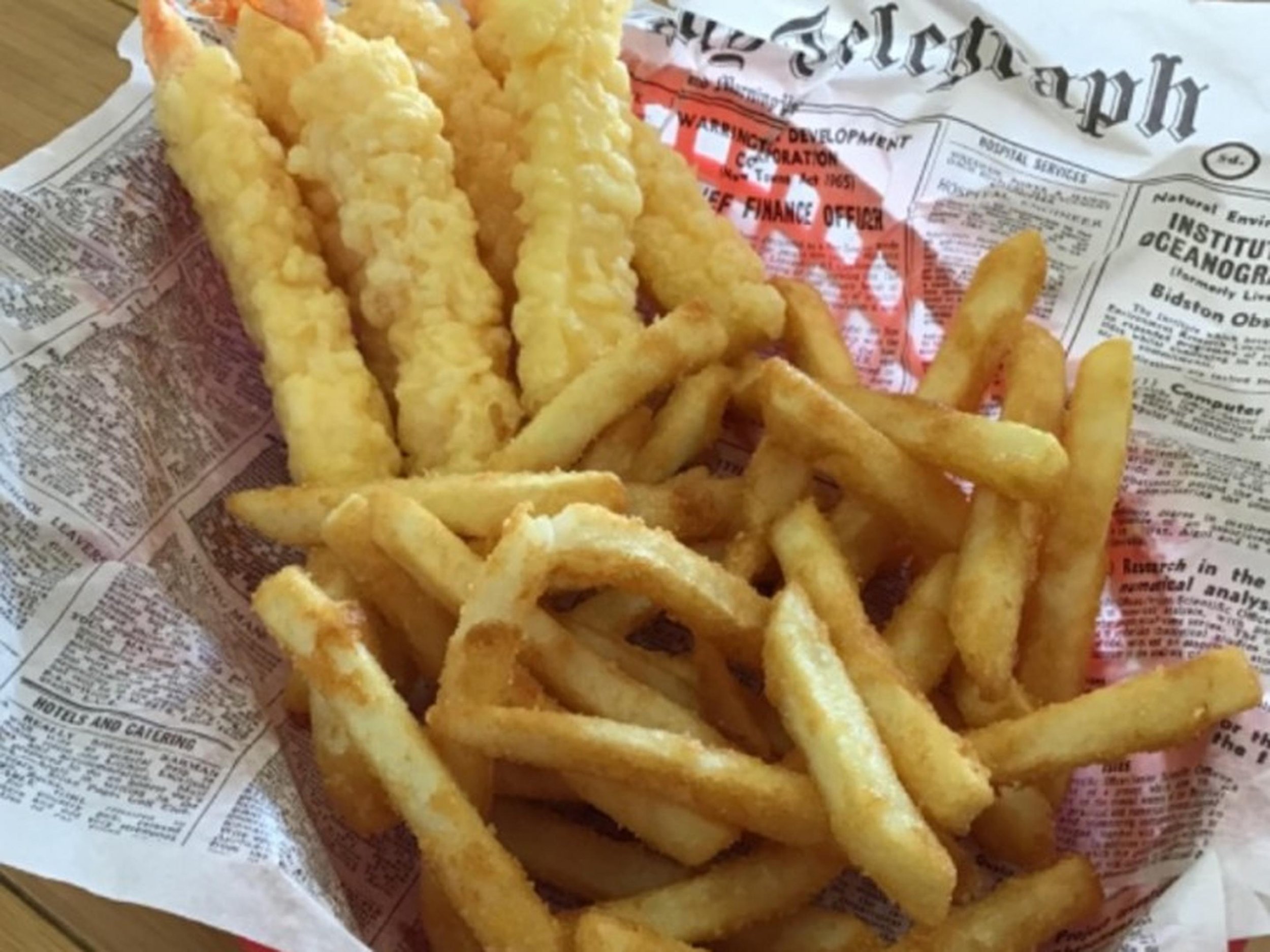 A basket of battered and fried fish filets and French fries on newspaper-lined basket.