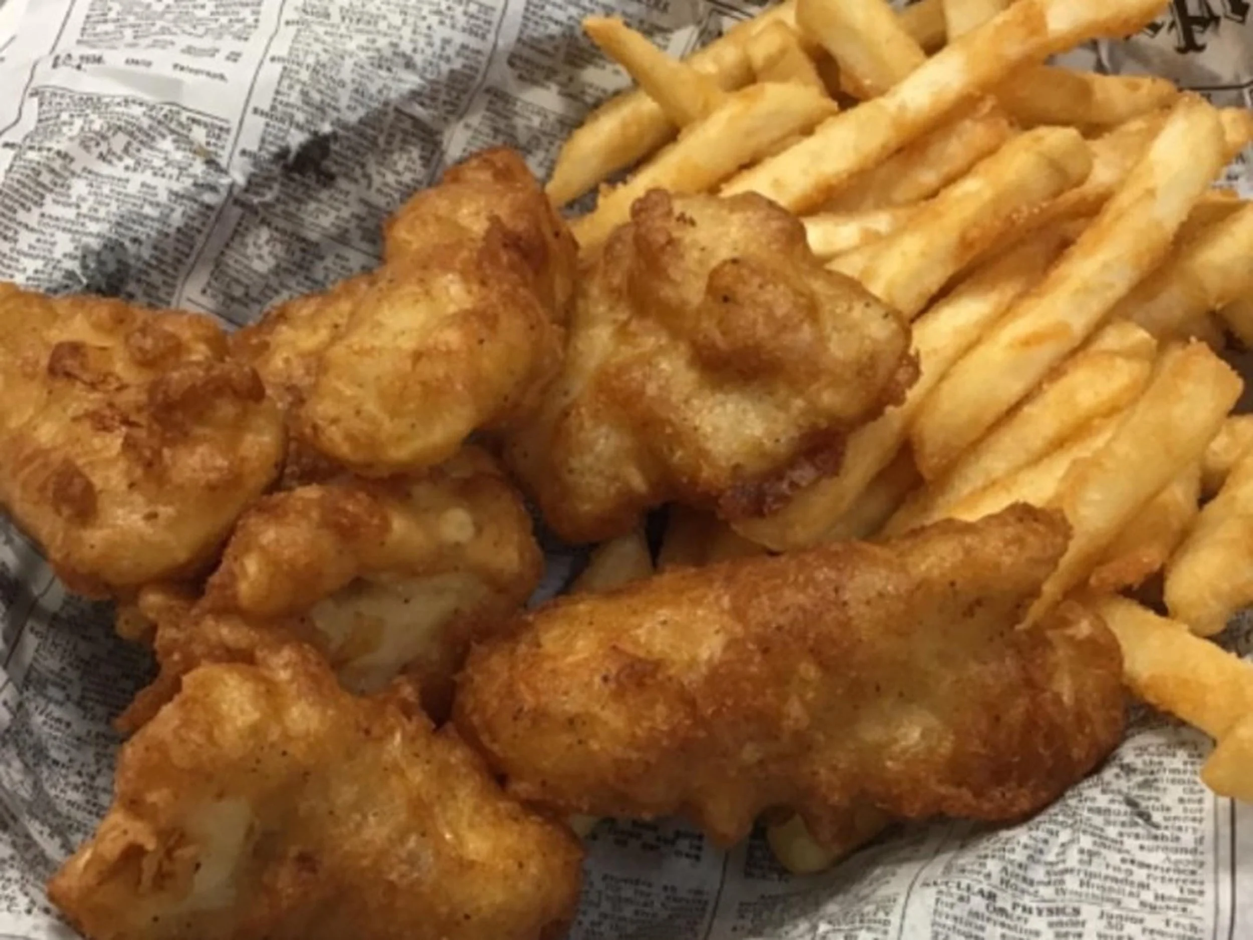 Golden fried chicken drumsticks and crinkle-cut French fries on newspaper-wrapped tray.