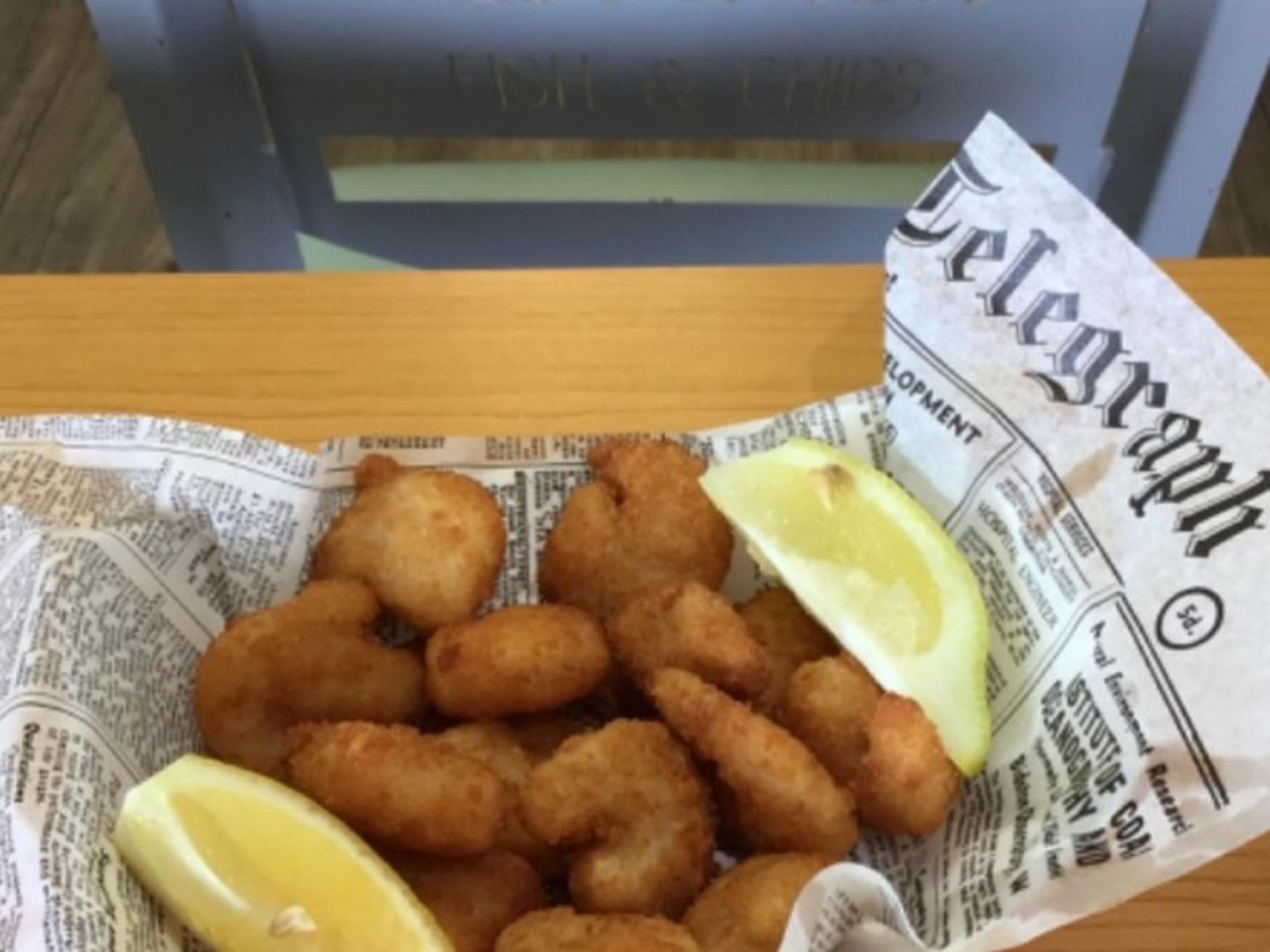 Fried fish bites served with lemon wedges, placed on newspaper-lined tray.
