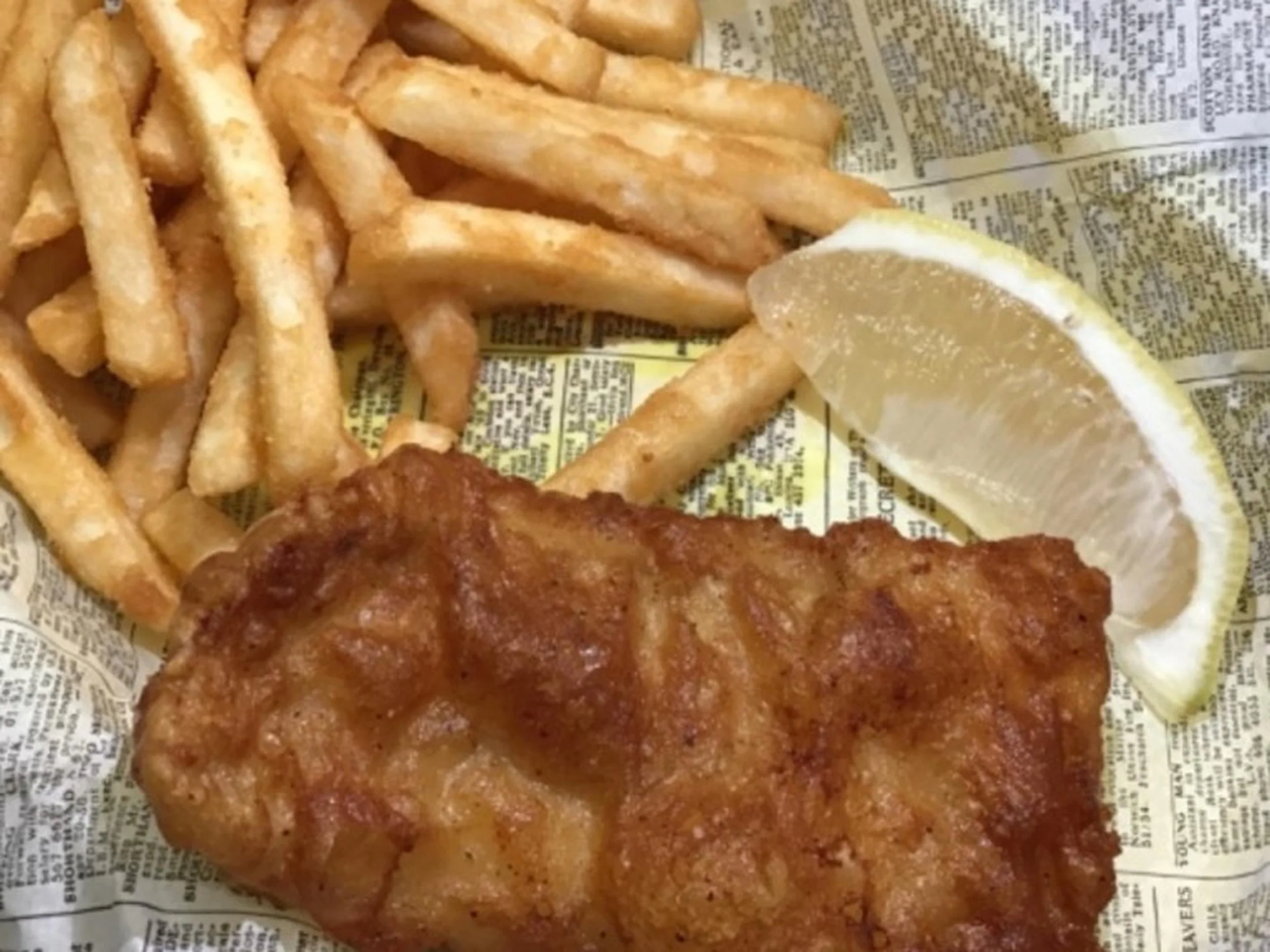 Fried French fries with a lemon wedge on newspaper